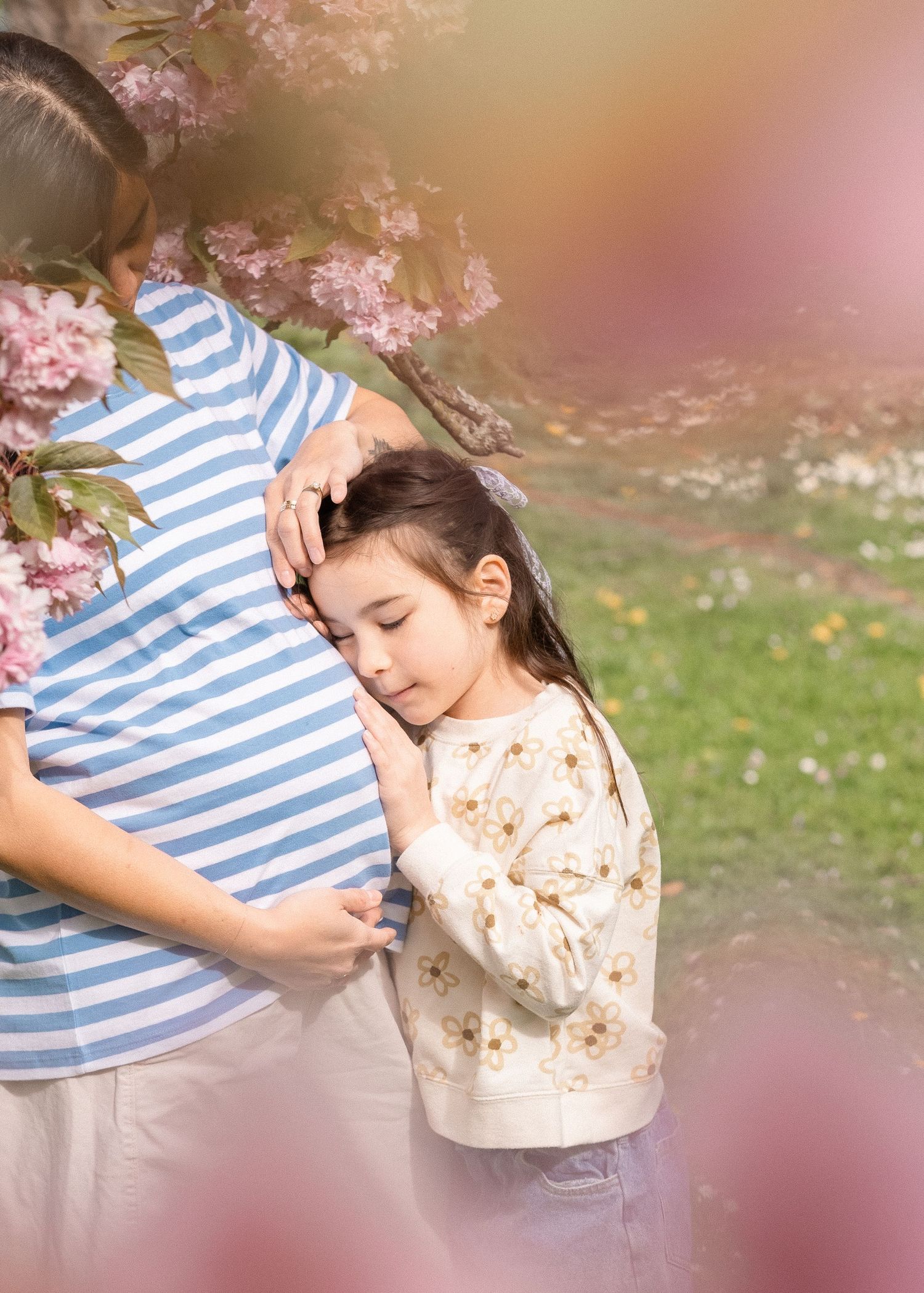 A gentle moment captured under cherry blossoms with soft pink bokeh effects in the background.