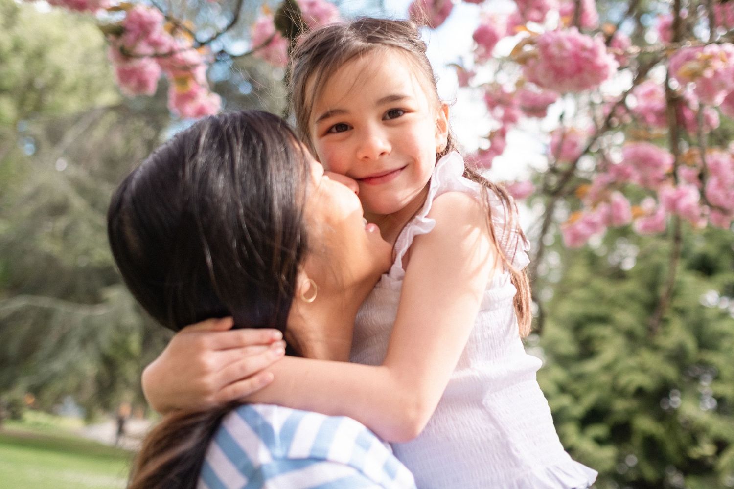 A couple shares tender moments under blooming cherry blossom trees in a spring garden setting.