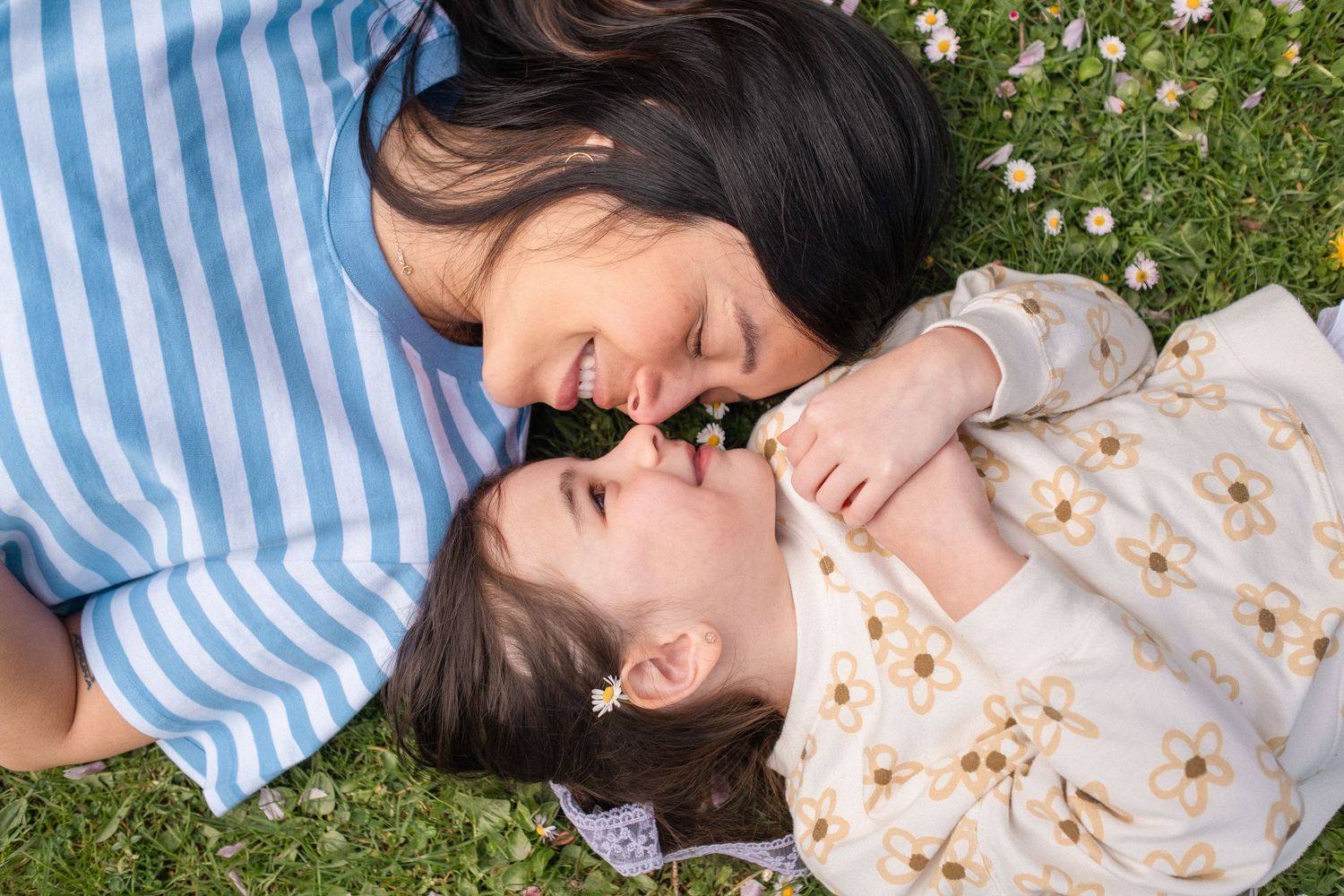 Person in striped shirt and floral dress relaxing on grassy lawn.