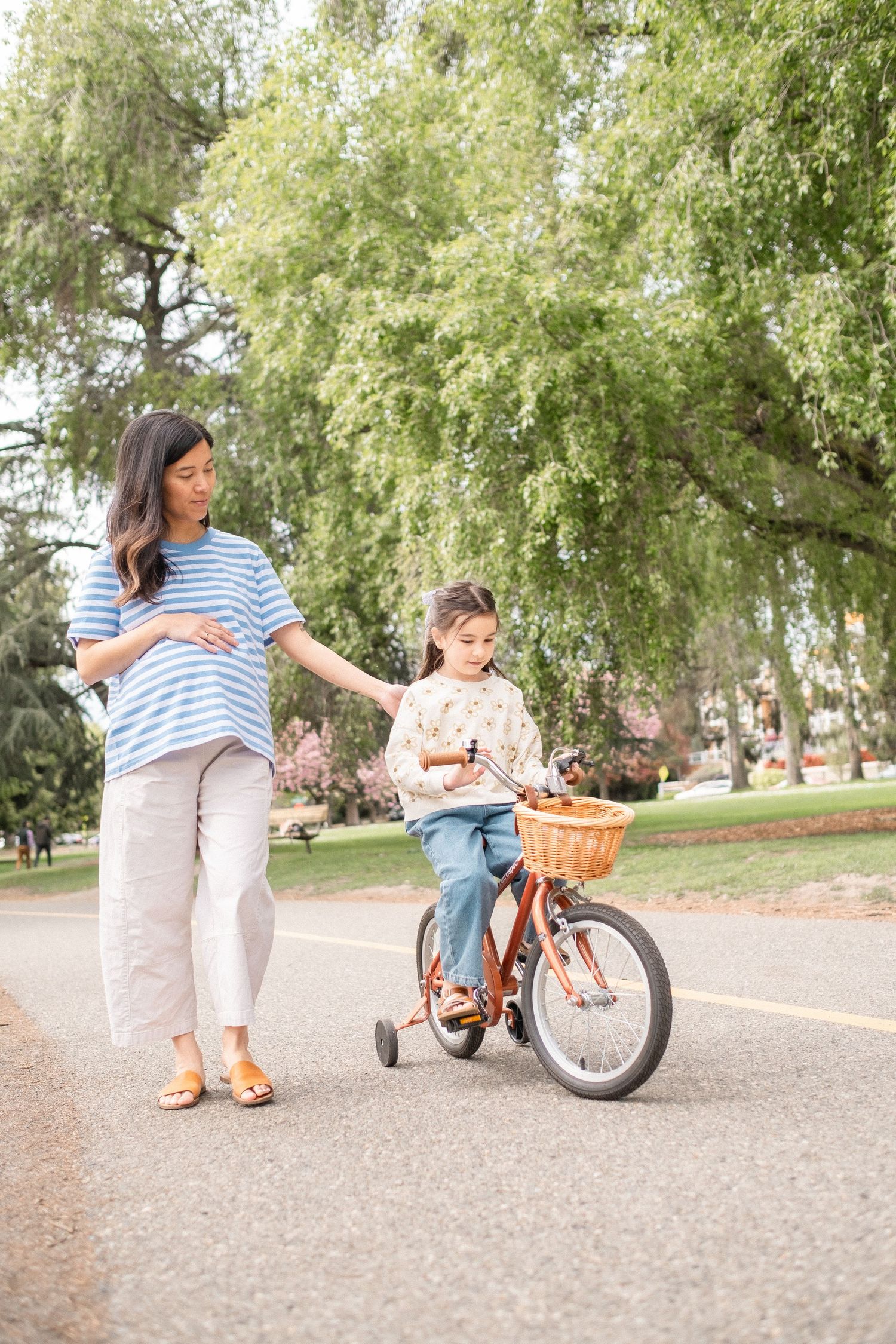 A vintage orange bicycle being adjusted on a paved path under green trees.