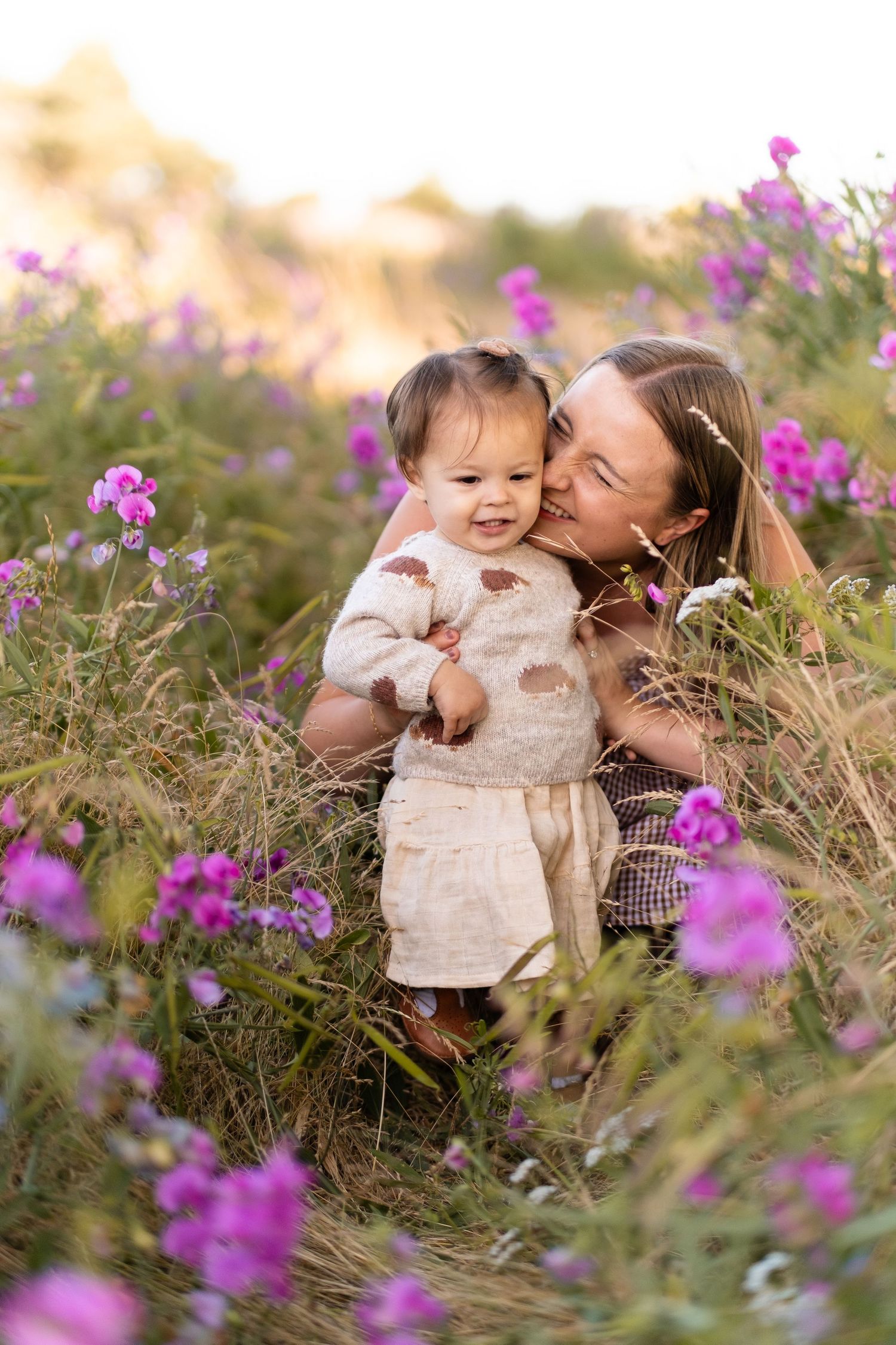 Sweet outdoor portrait of tender moment surrounded by blooming purple wildflowers in warm golden light.