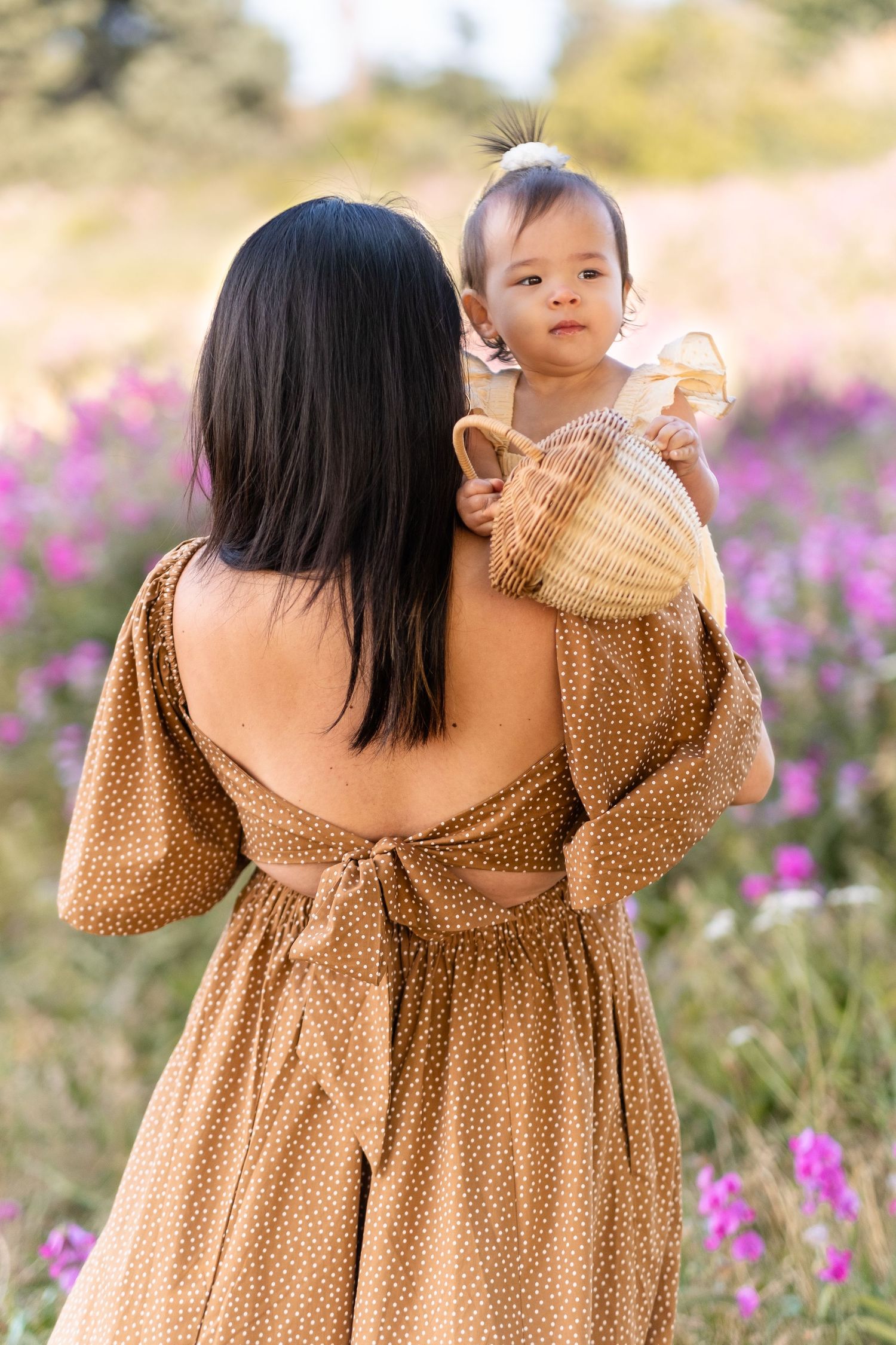 Two people in brown polka dot dress standing in a field of purple wildflowers on a sunny day.