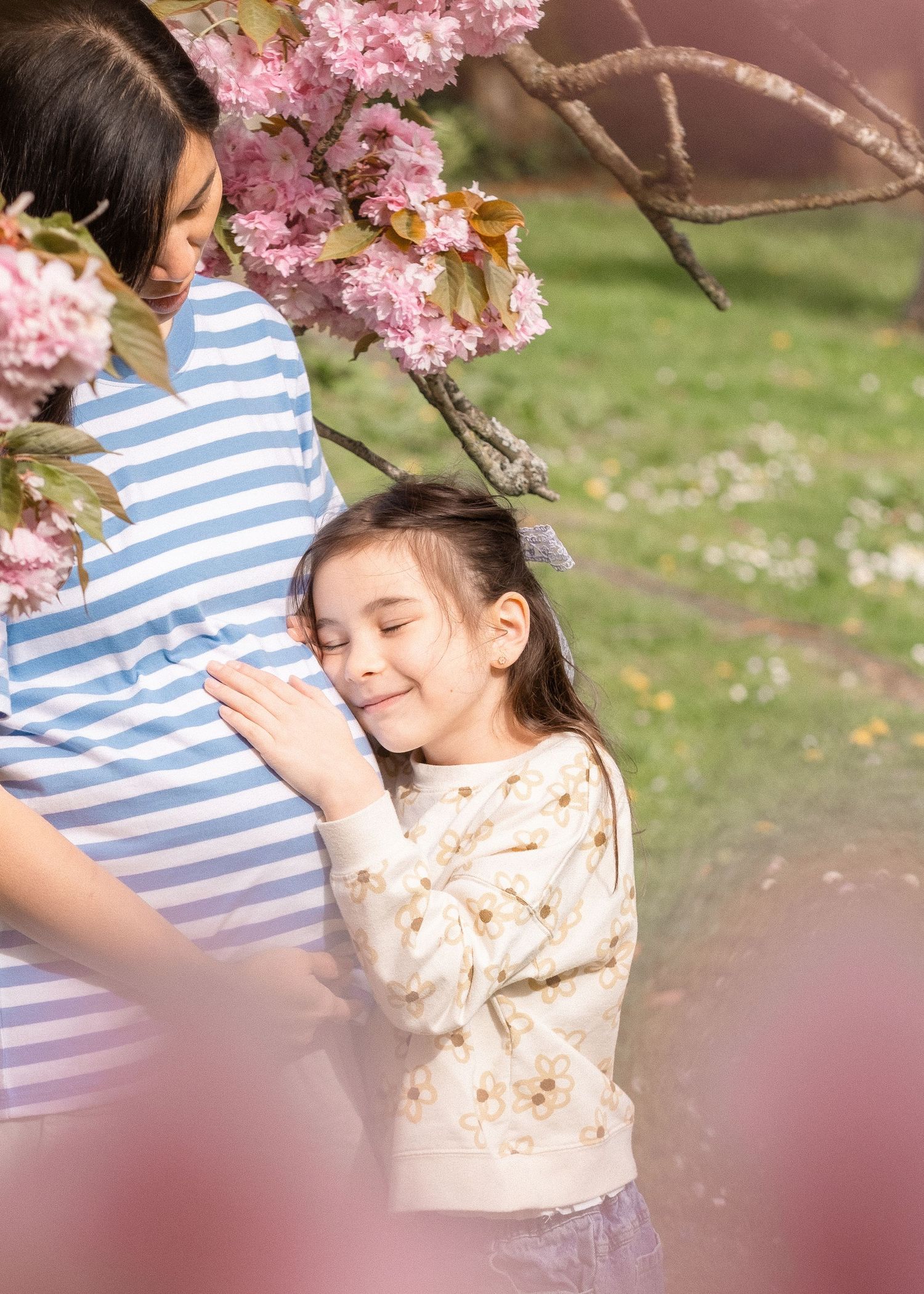 A playful spring photoshoot beneath blooming pink cherry blossom trees in casual striped and floral attire.