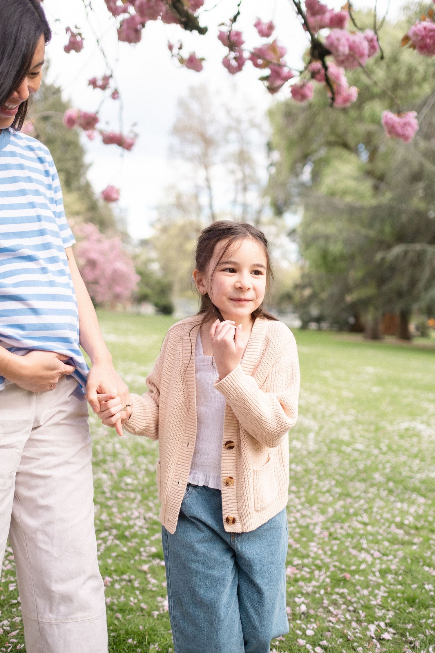 A spring photoshoot in a field of daisies with pink cherry blossoms overhead and casual outfits in blue and beige.