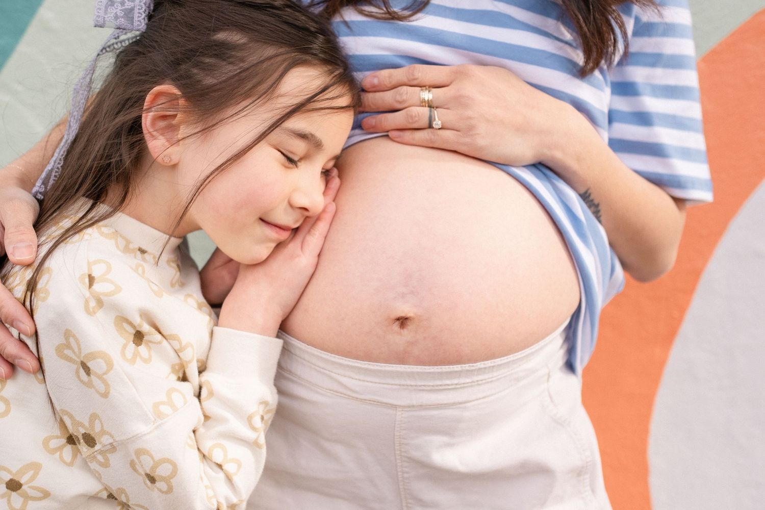 Close up of a pregnant belly being lovingly embraced against a colorful background.