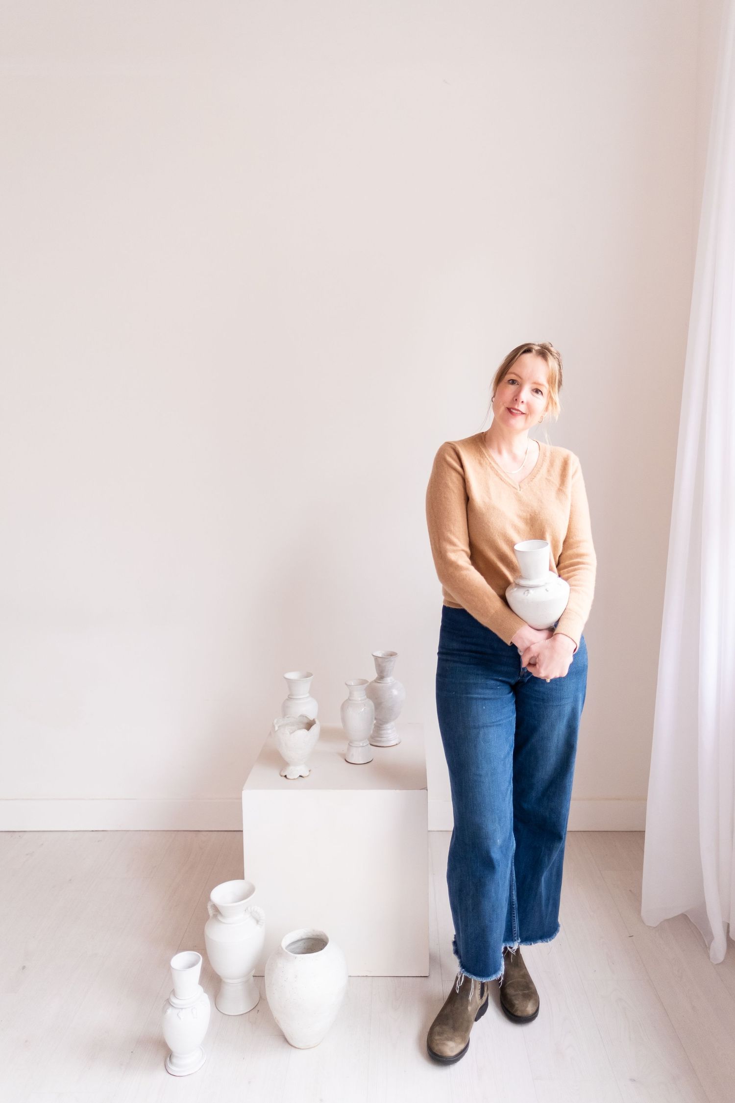 Contemporary studio scene with pottery artist standing beside white ceramic pieces on display.