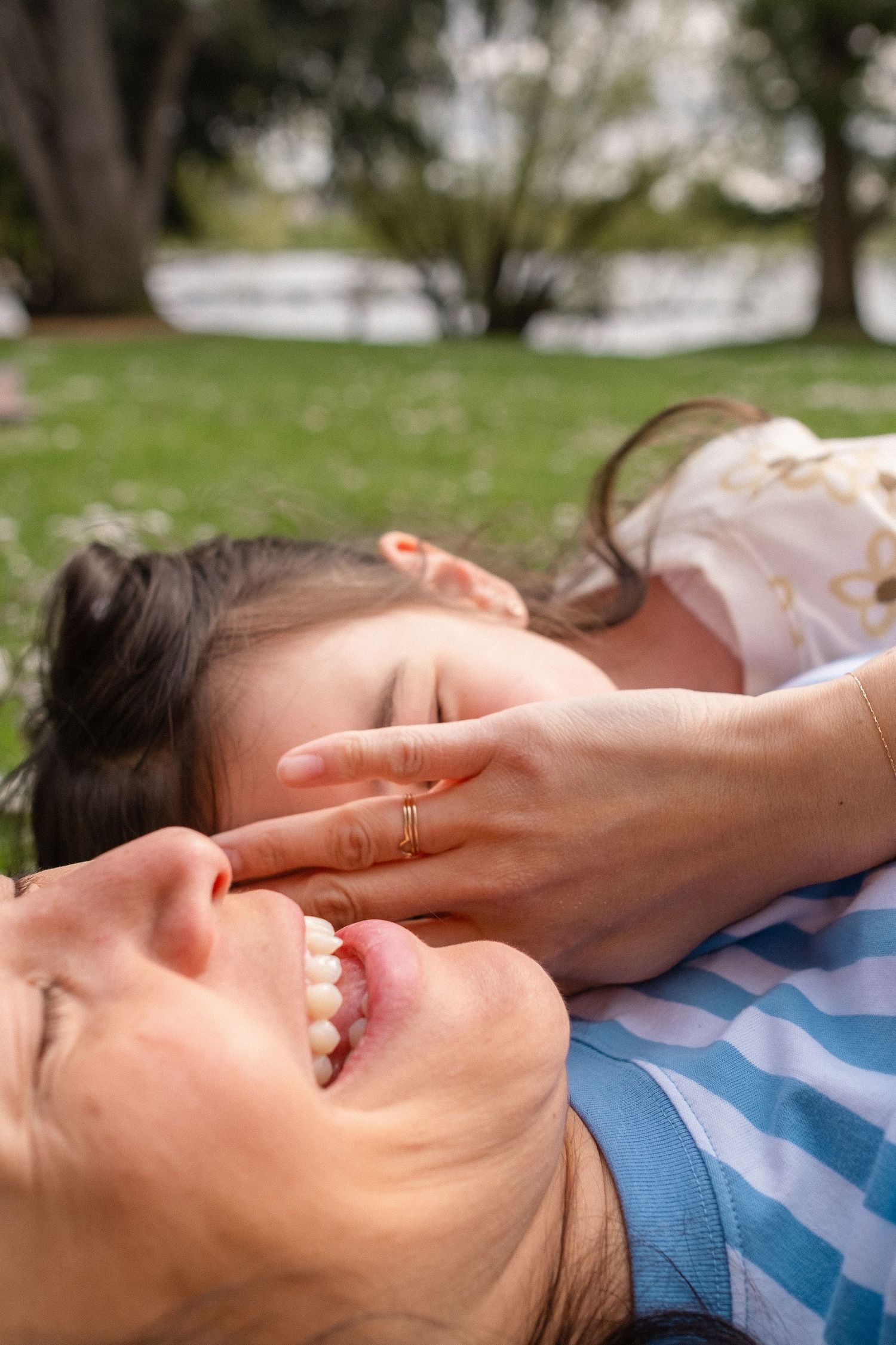Two people lying on grass outdoors sharing a joyful laughing moment together on a sunny day.