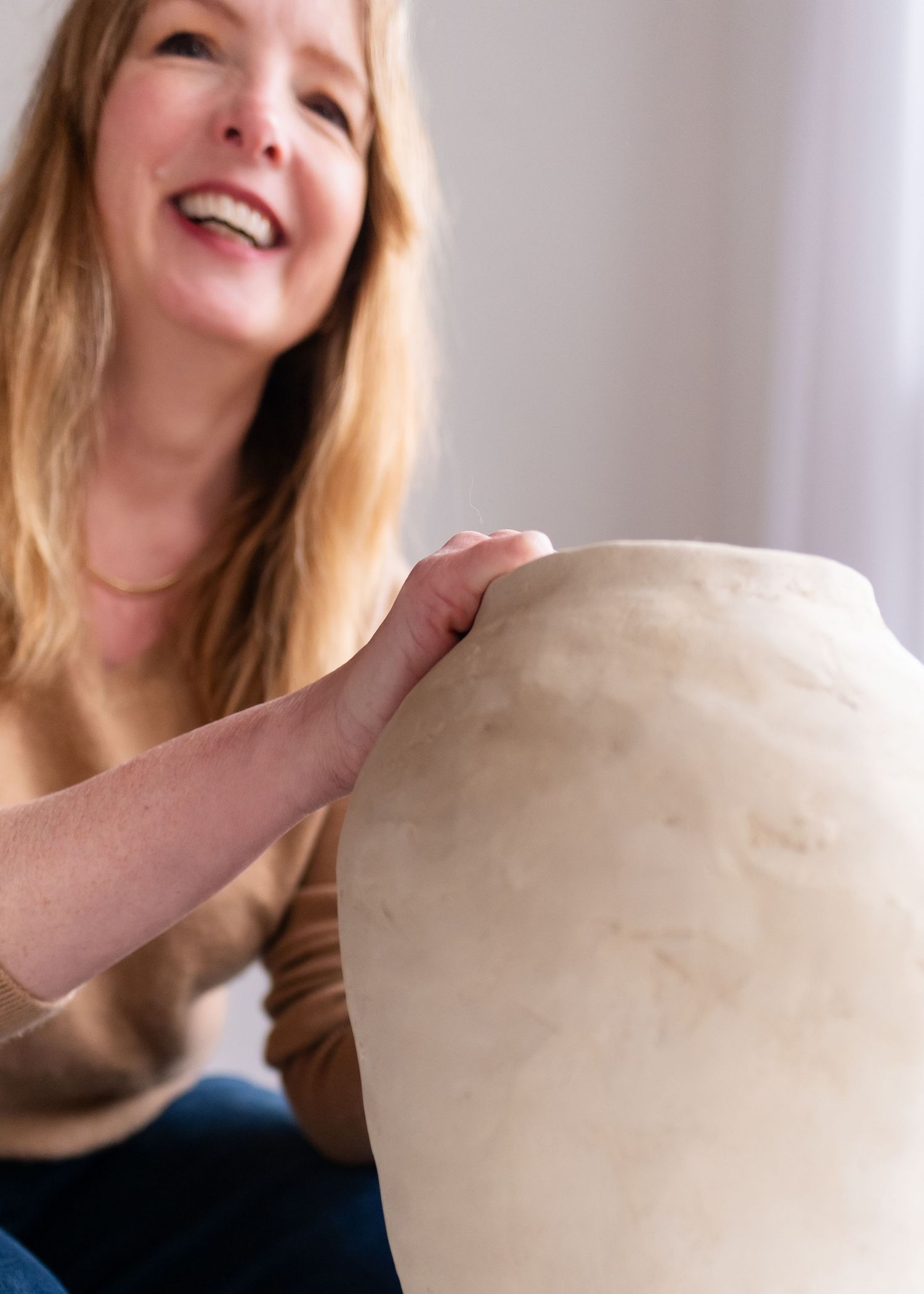 Person holding and examining a large white ceramic vase against a neutral background.
