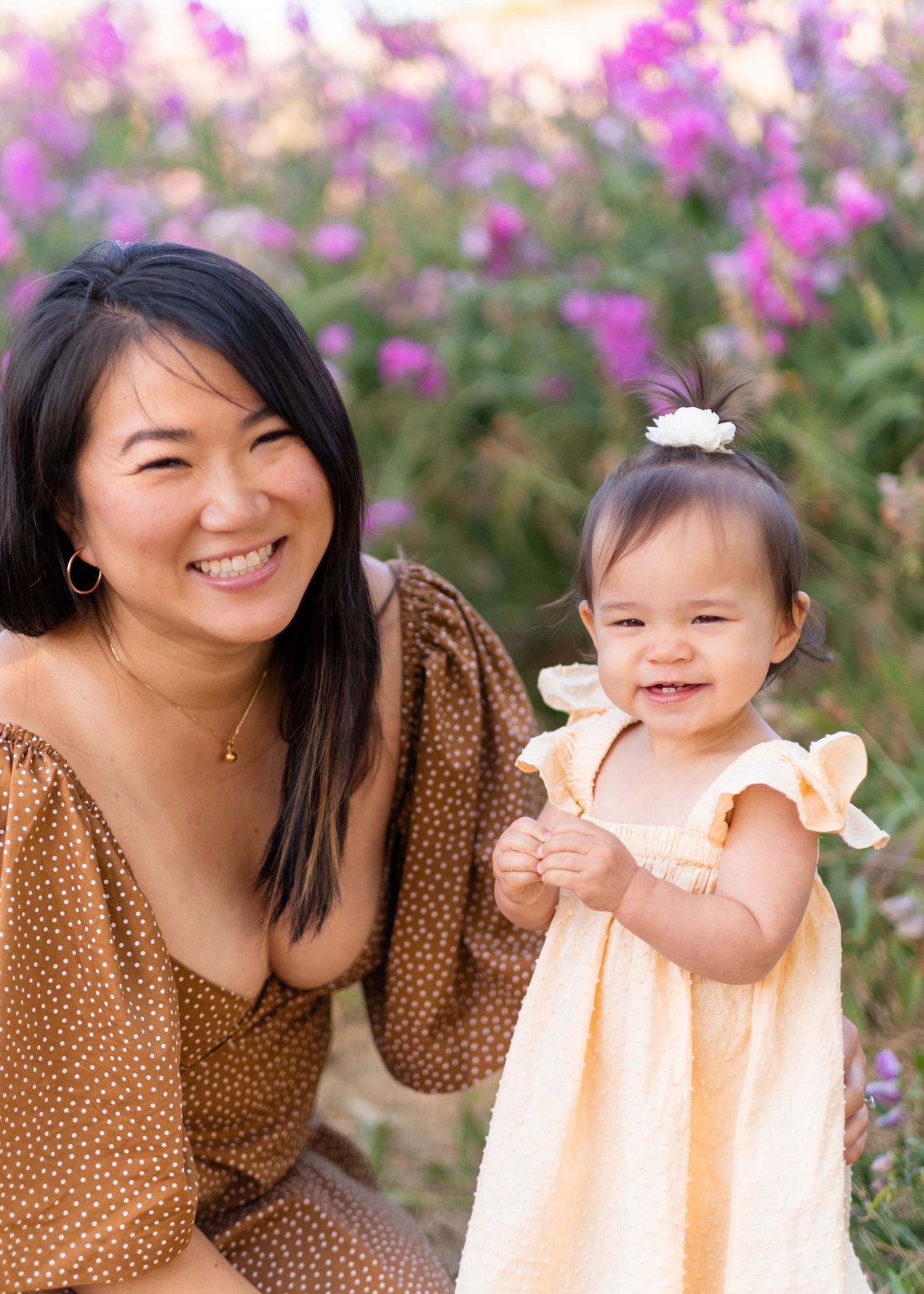 Two figures in coordinating brown and peach outfits share tender moments among blooming pink flowers in a garden setting.
