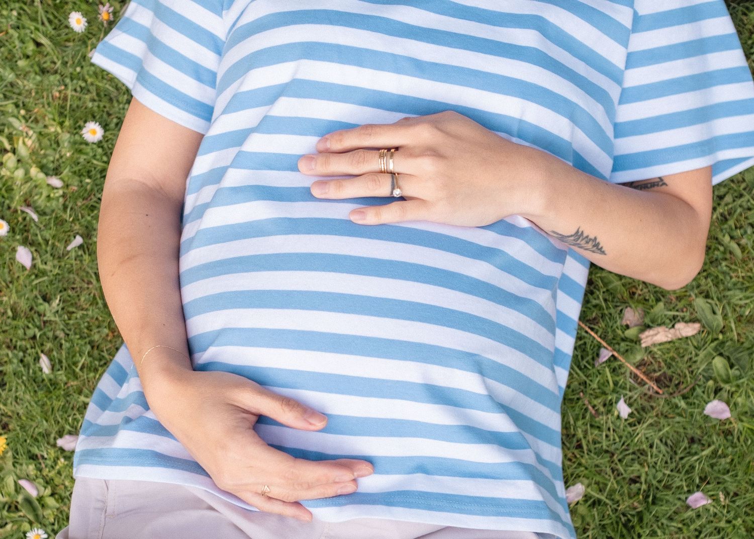 Person wearing blue and white striped shirt lying on grass in a park setting.