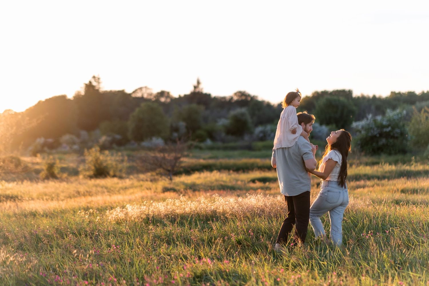 Two people stand together in a golden field at sunset with warm sunlight illuminating the peaceful rural landscape.