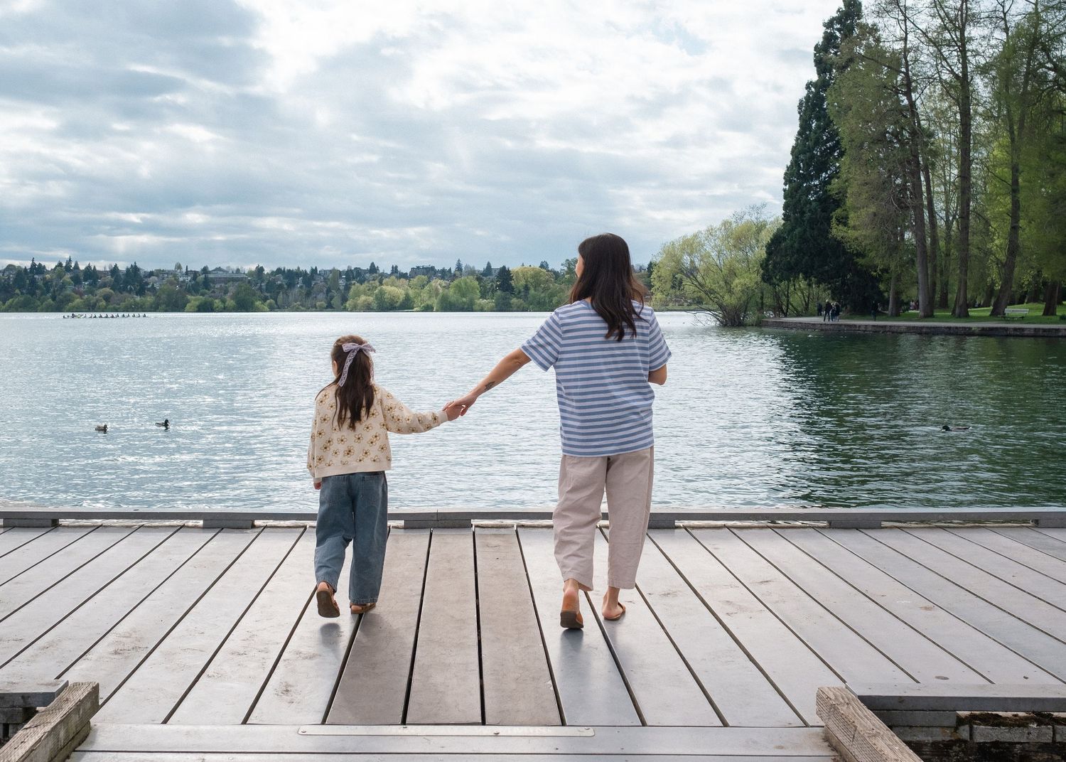 Two people sit together on wooden dock overlooking serene lake surrounded by trees.
