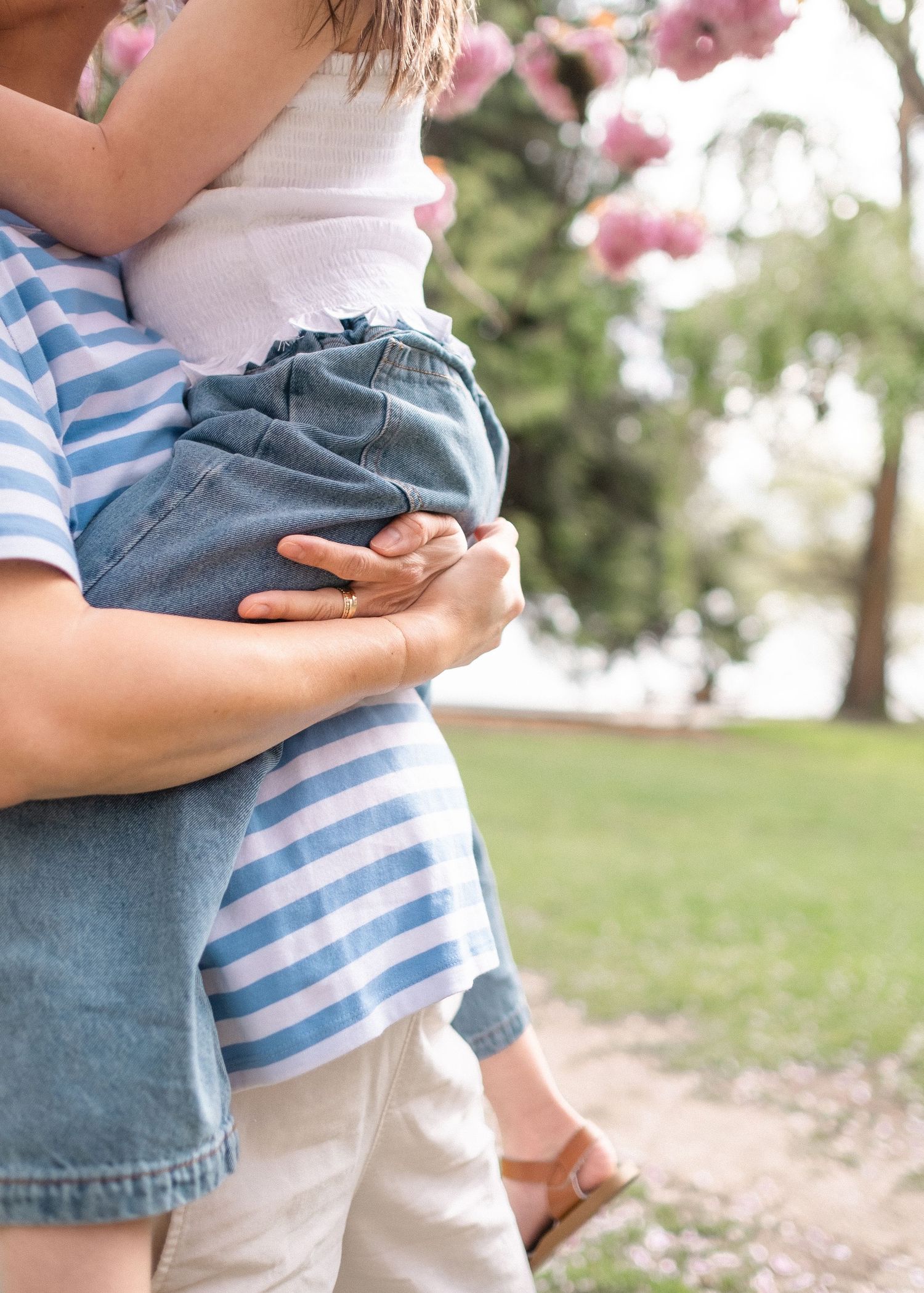 Close-up view of two people hugging, one wearing striped blue shirt and other in denim, against blurred pink blossoms.