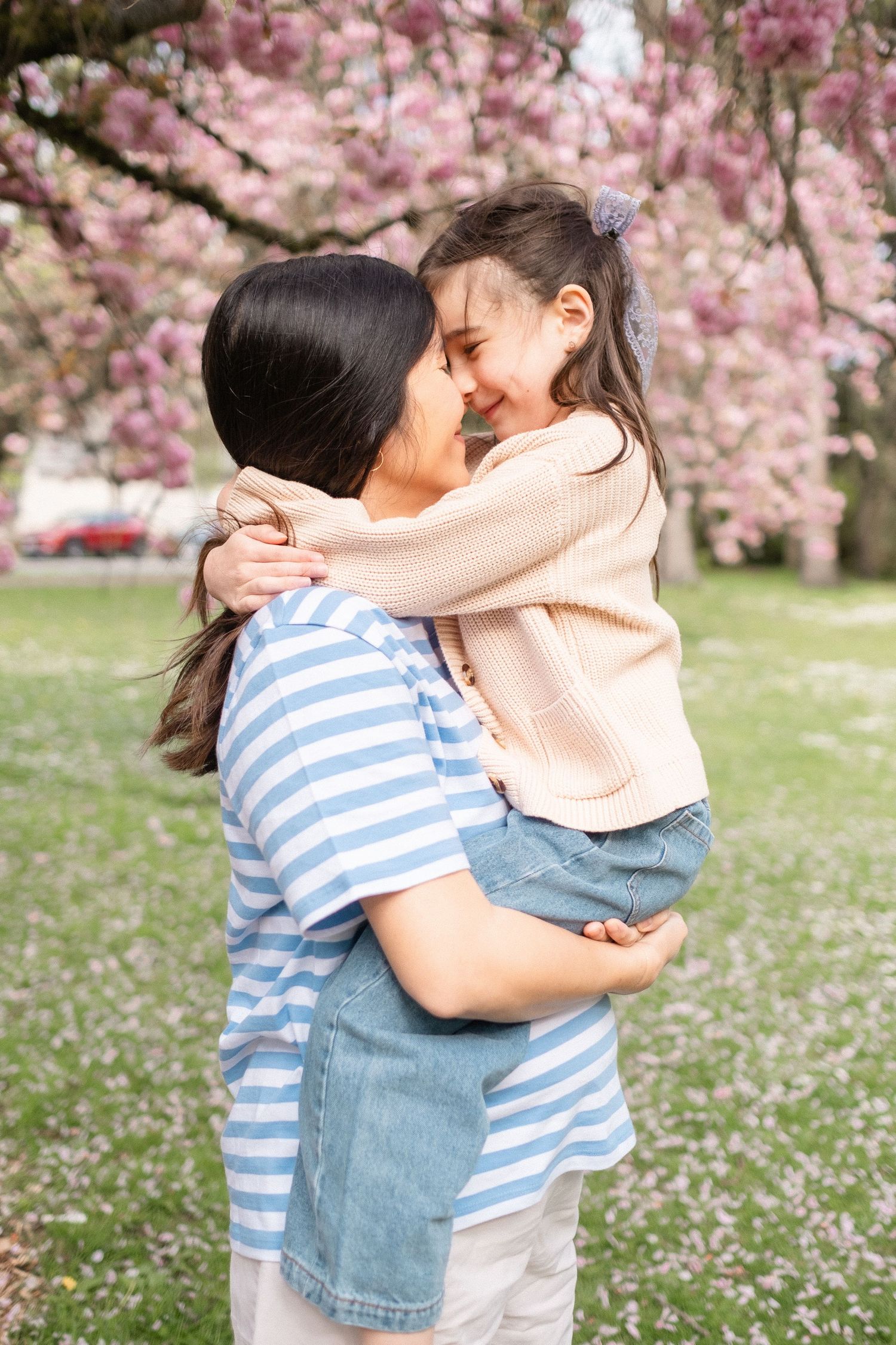 Two people embrace under blooming pink cherry blossom trees in a springtime garden setting.