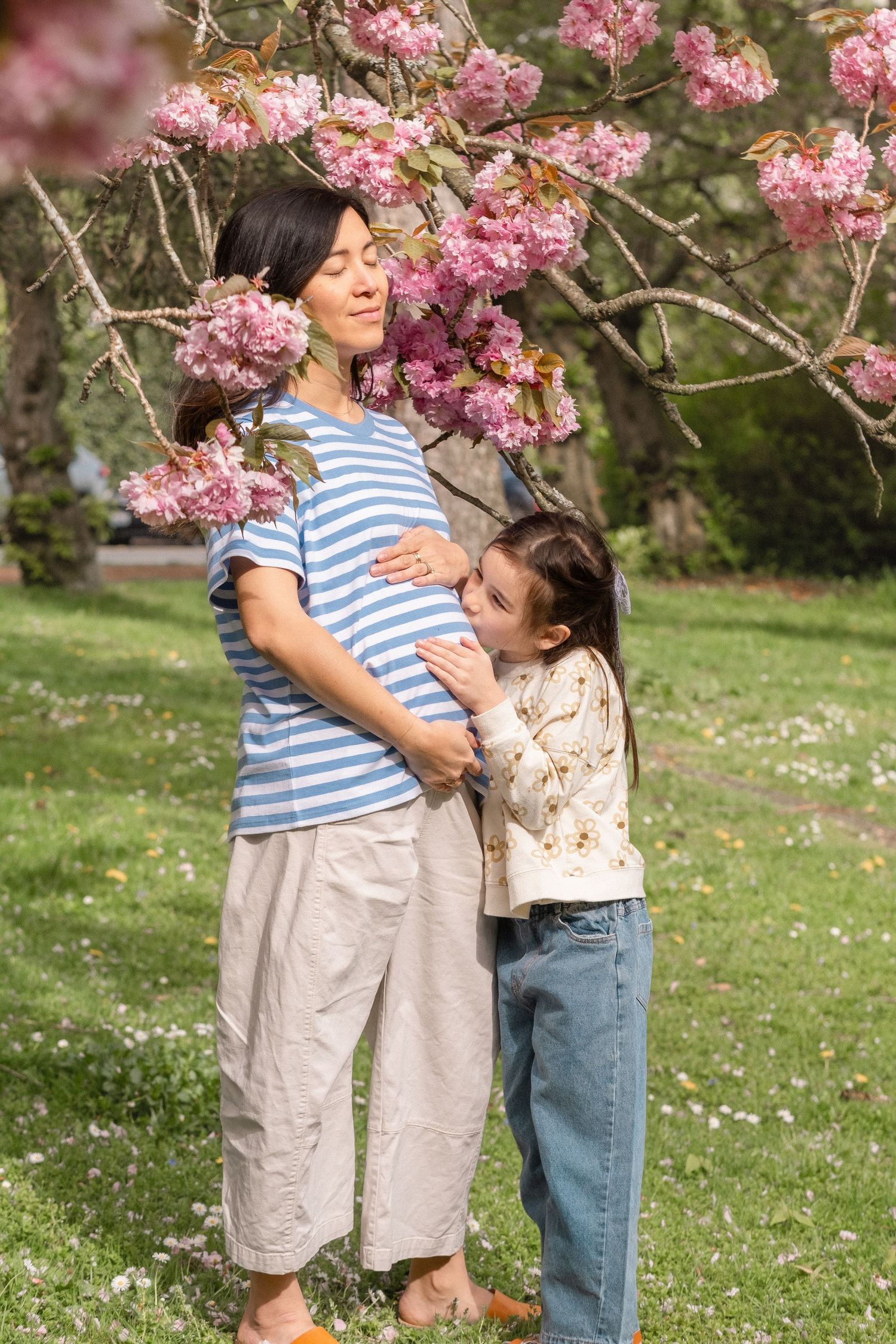 People share a joyful moment beneath pink cherry blossoms with scattered petals on the ground.