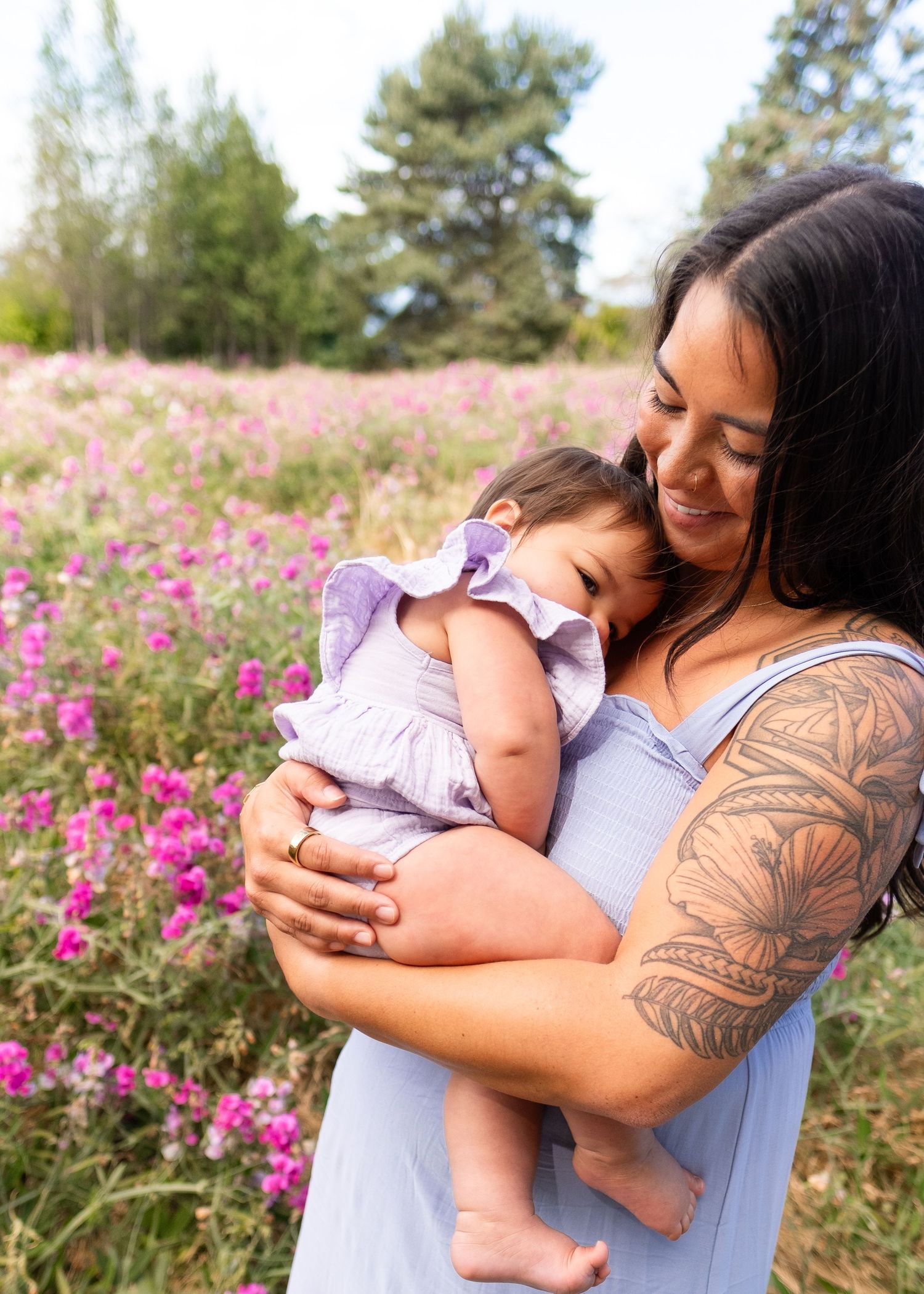 A tender moment shared between parent and baby in a field of vibrant pink wildflowers on a sunny day.