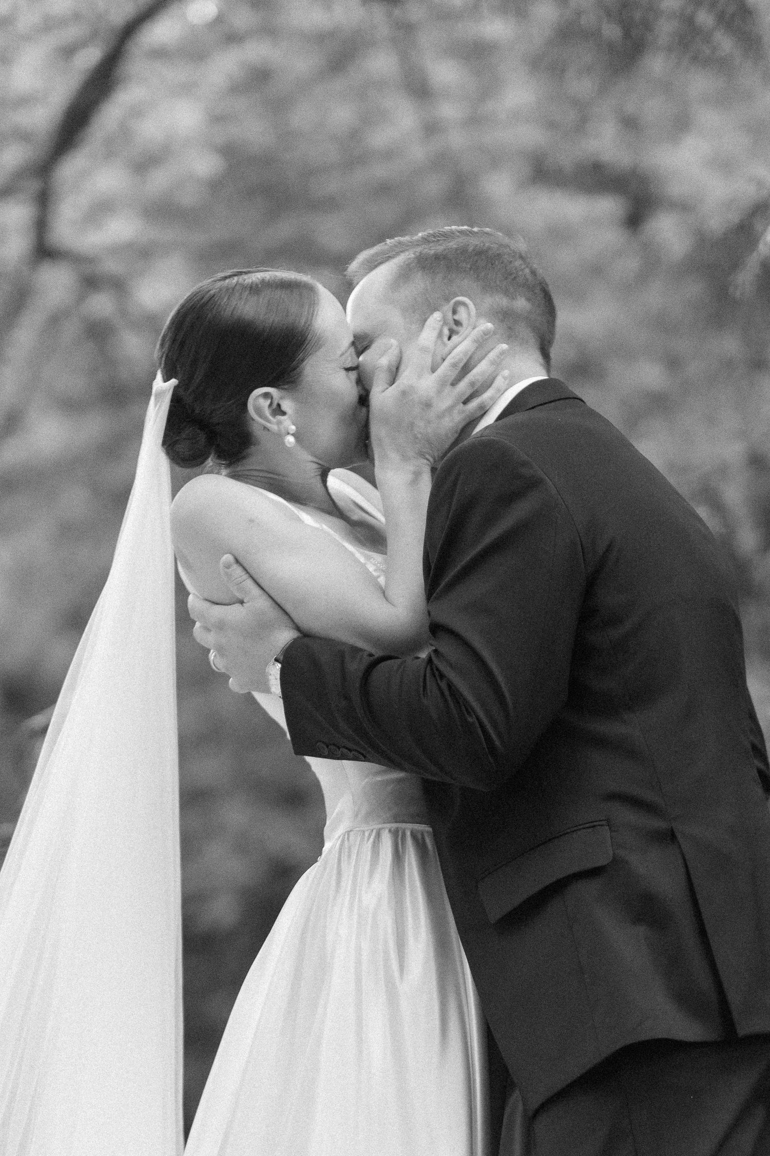 Black and white photo of a bride and groom sharing their first kiss at a wedding ceremony.