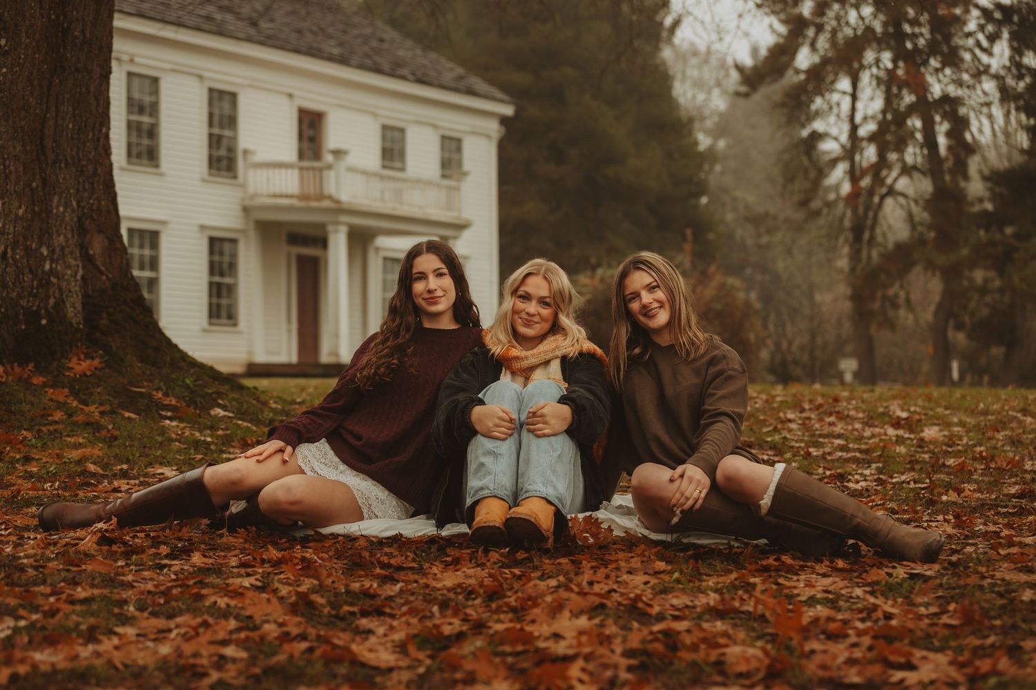 Friends lounging together on autumn ground with matching socks near a historic white building.