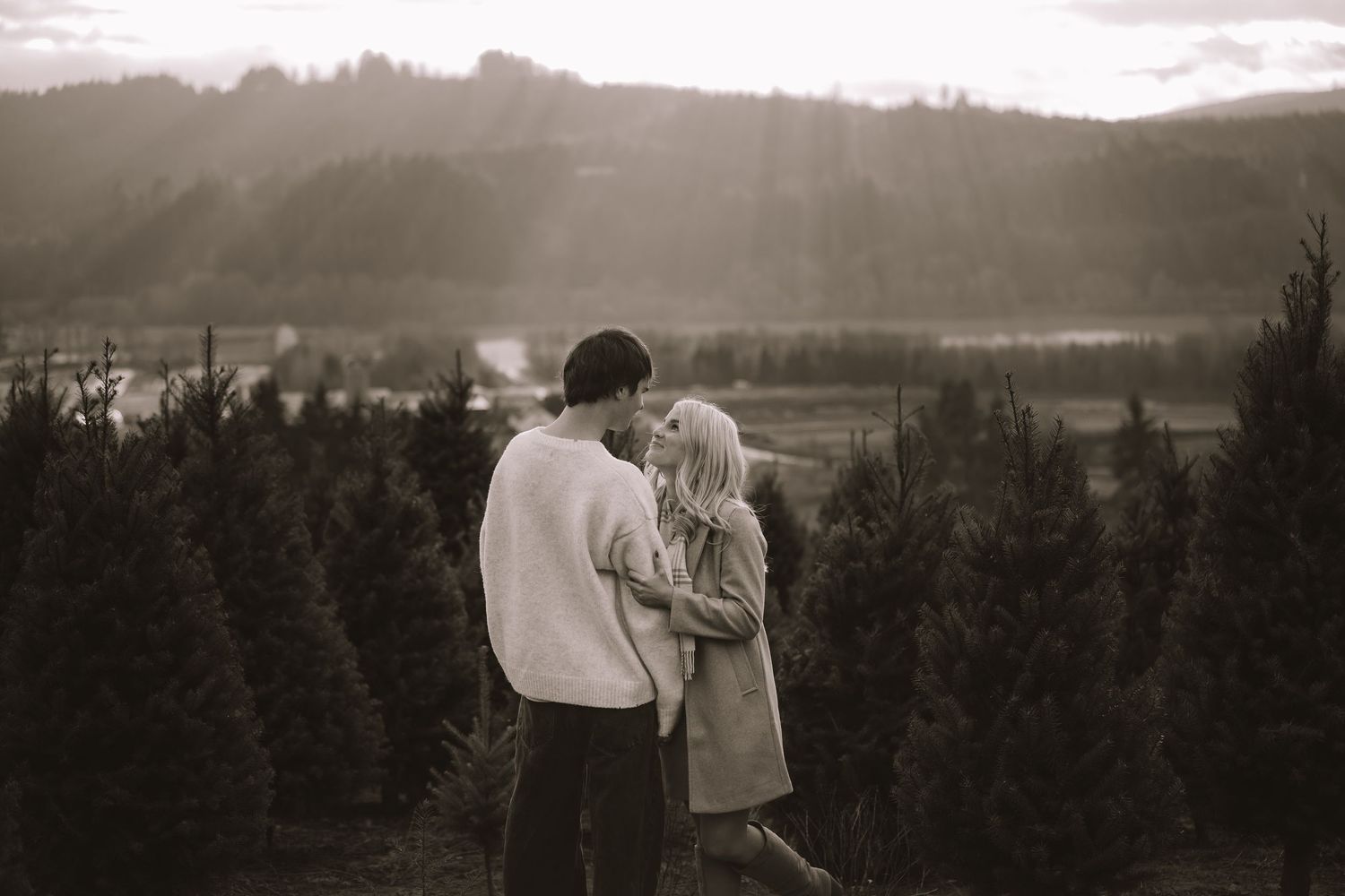 Silhouetted couple embraces against a moody mountain landscape at sunset with dramatic clouds.