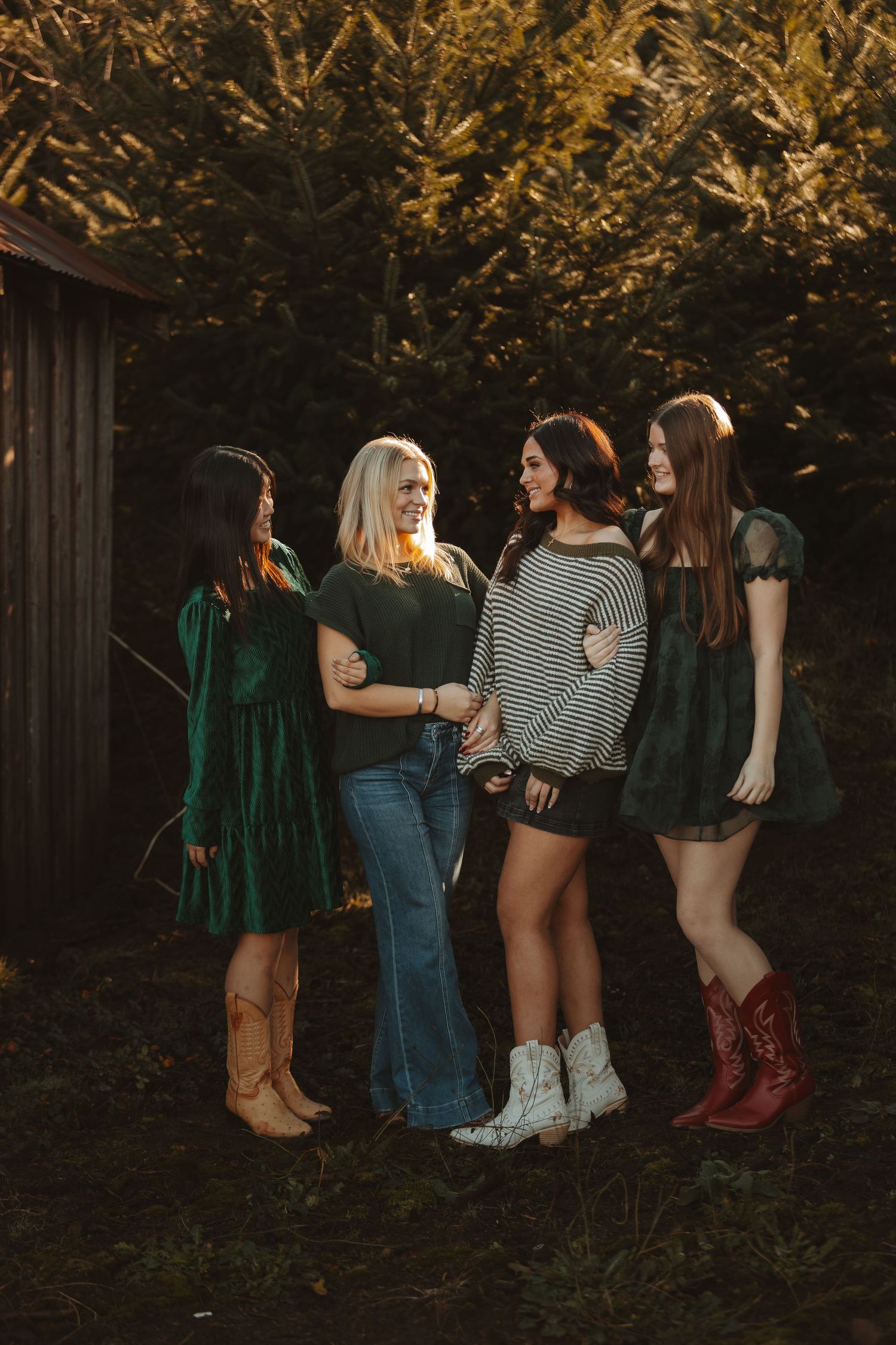 A group poses together in casual outfits and cowboy boots against a rustic outdoor backdrop at sunset.