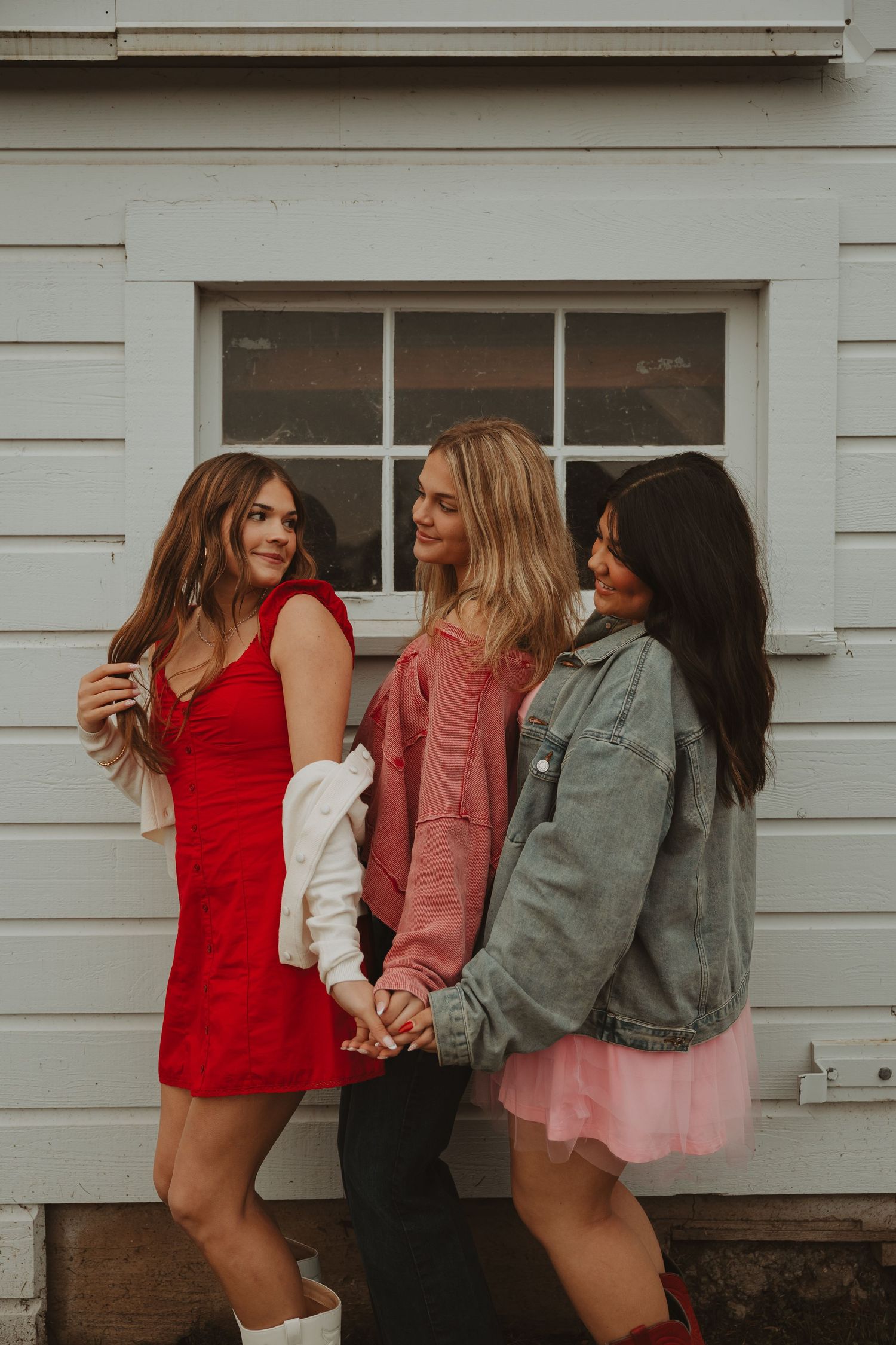 A group of friends in casual outfits dance and laugh together against a white wall background.