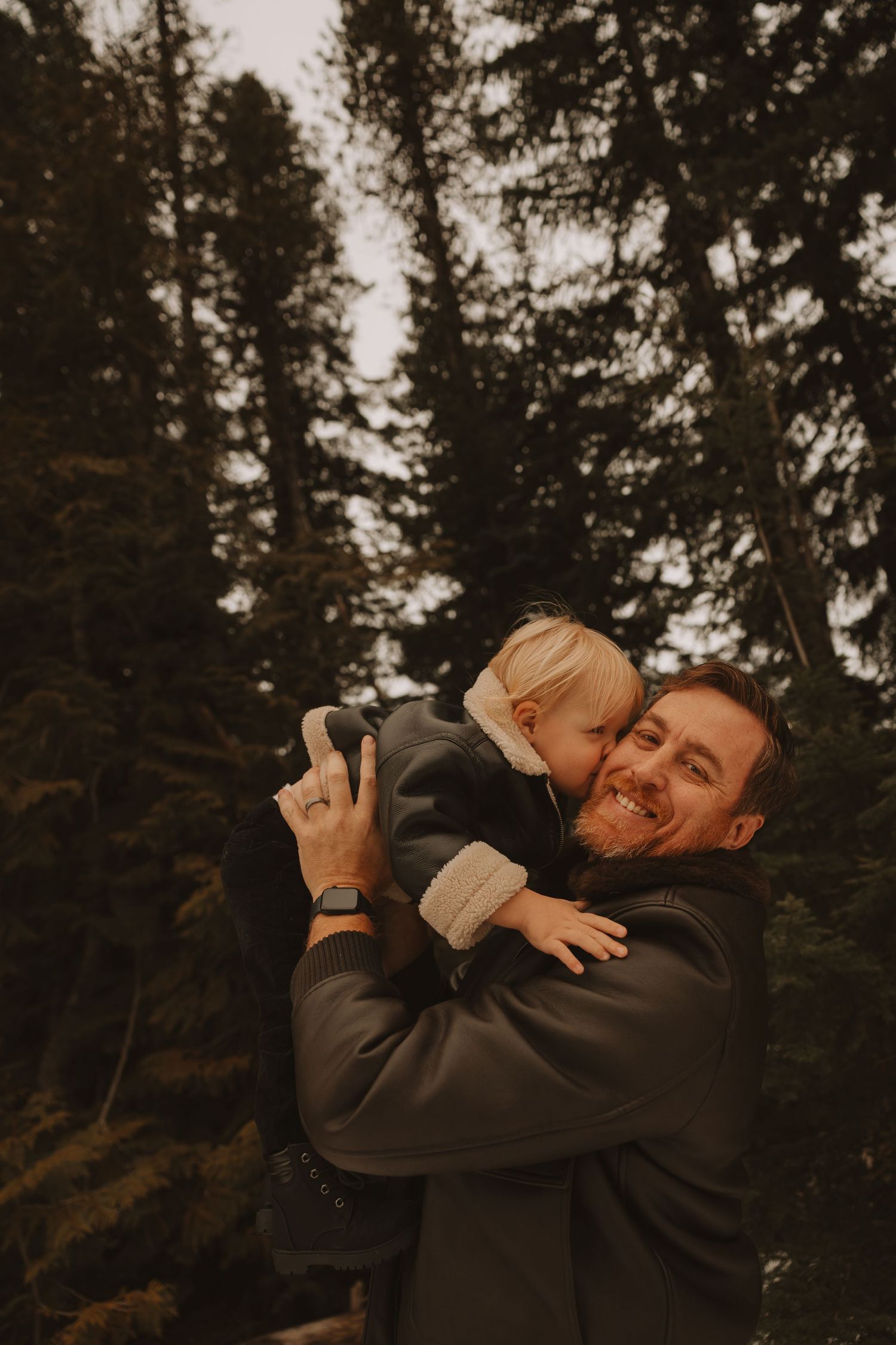 A loving embrace between two people against a backdrop of evergreen trees at sunset.