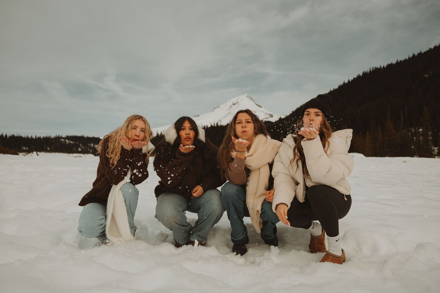 Four women posing and blowing snow in a winter mountain landscape.