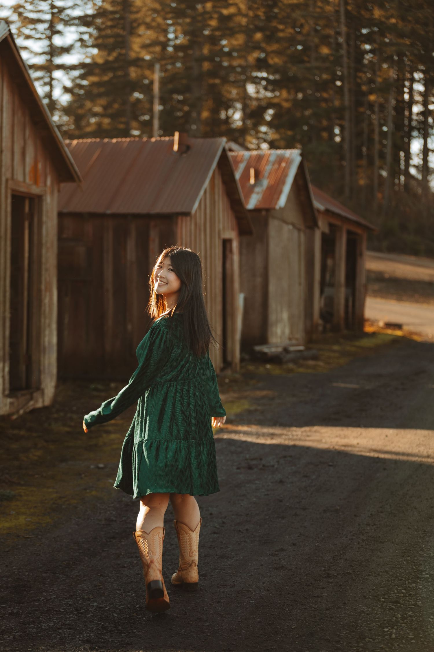Person in green dress twirls in front of rustic wooden cabins at golden hour.