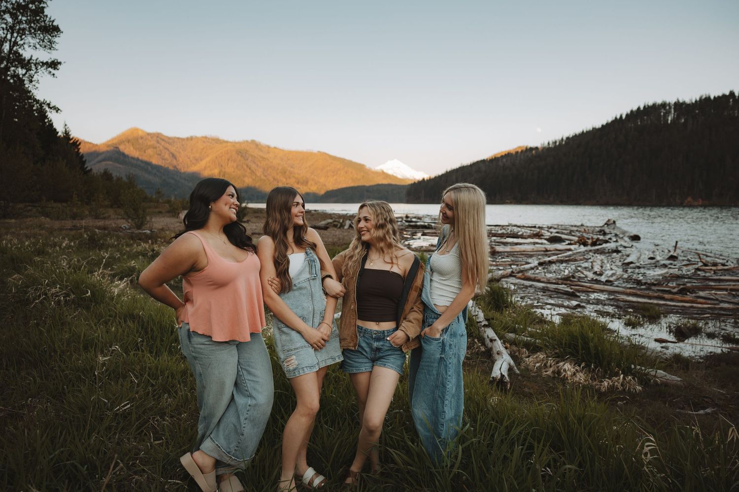 Four young women standing together by a mountain lake during a beautiful sunset.