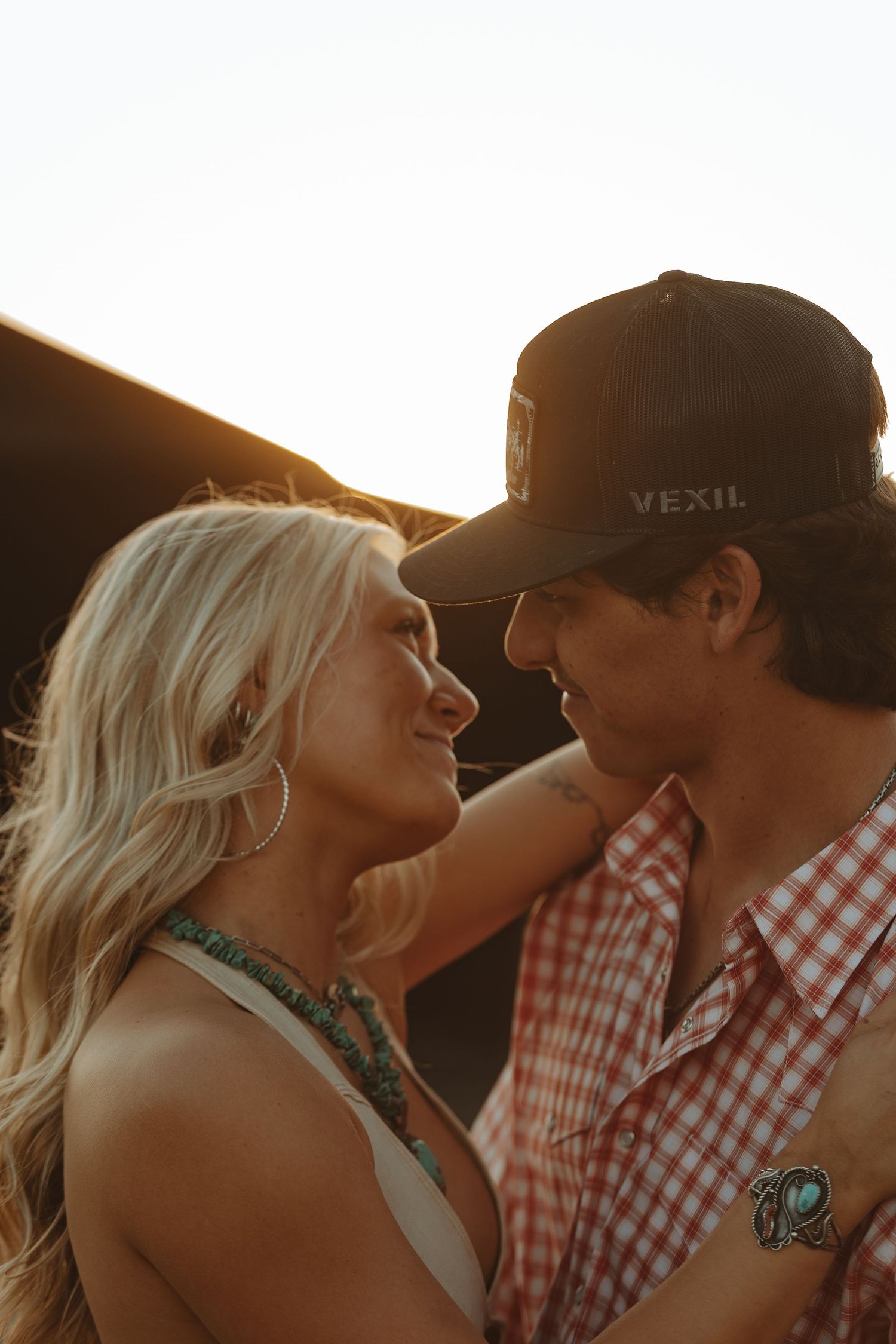 Blonde woman and man in a Vexil cap sharing an intimate moment at sunset on a farm.