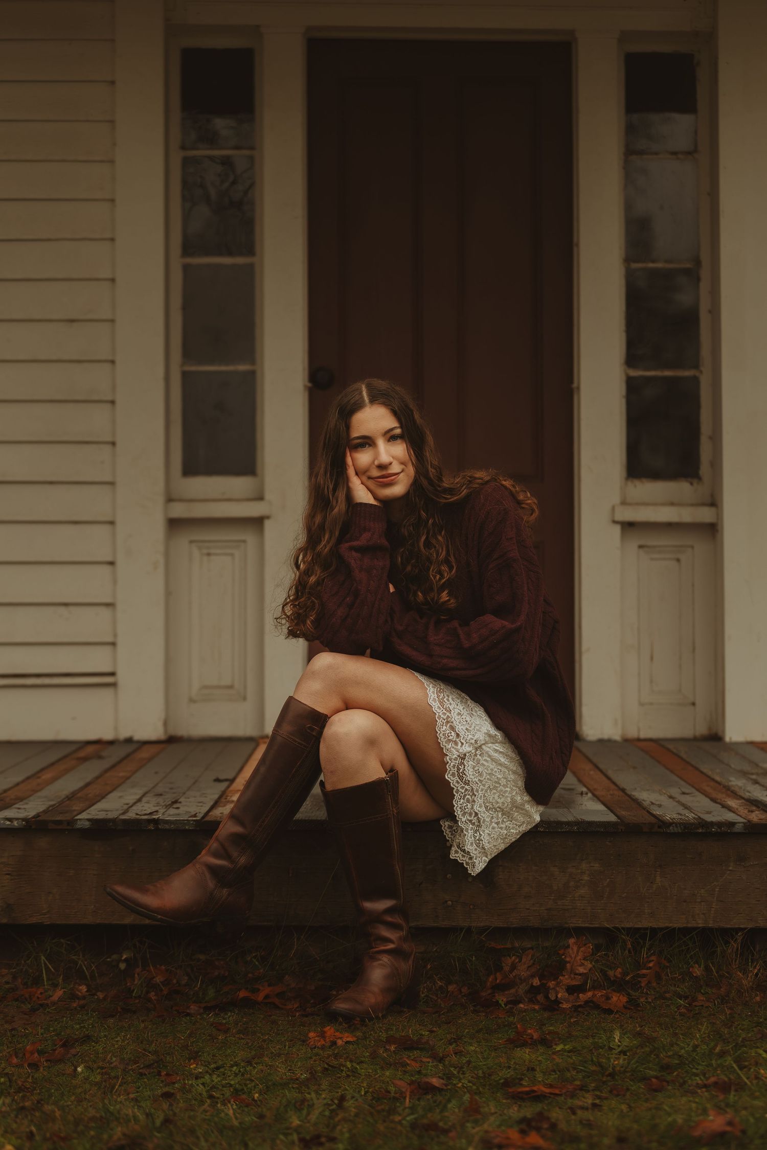 Person in white dress and brown boots lounging on wooden porch steps during autumn.