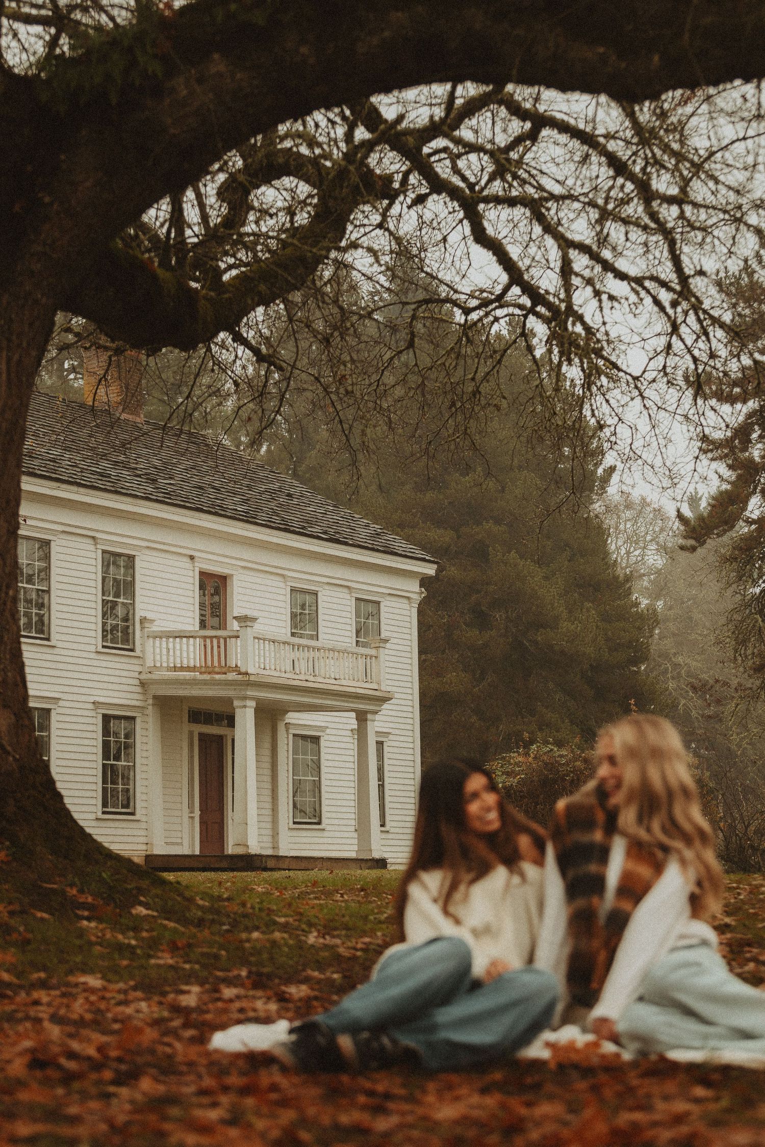 Friends relaxing together on autumn leaves in front of a white colonial house.