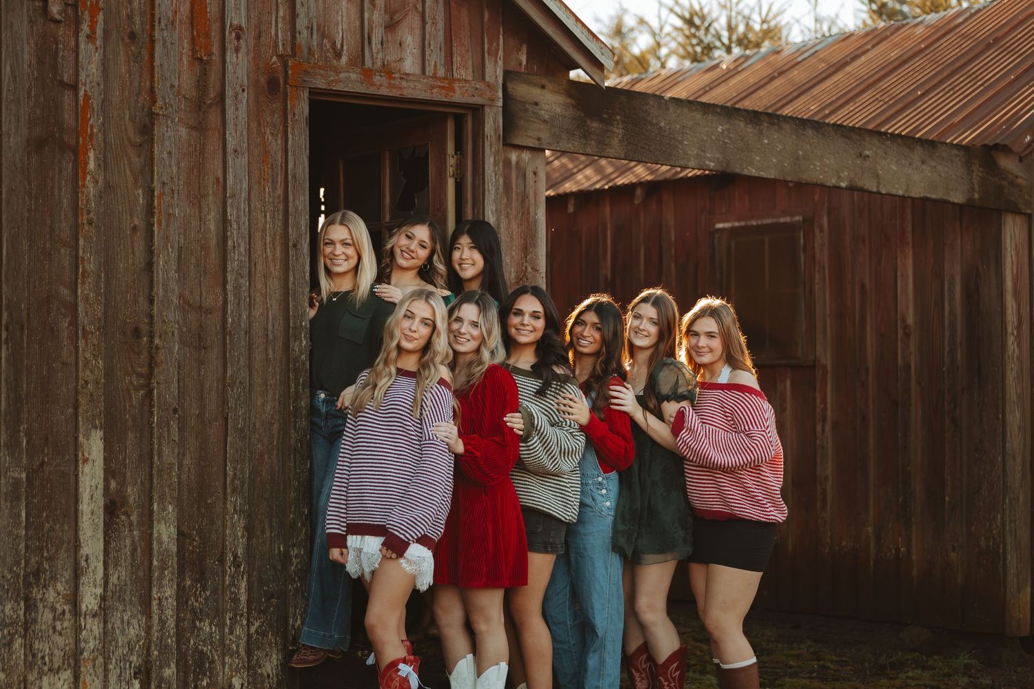 A group of friends pose together in casual outfits against a rustic wooden barn backdrop.
