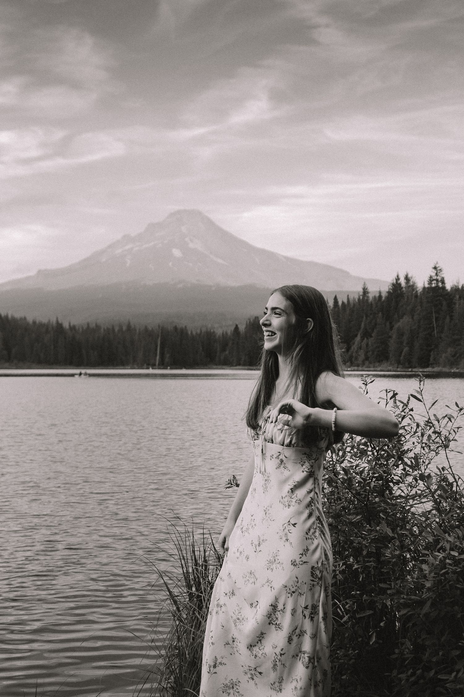 A person in a floral dress stands by a serene lake with Mount Hood visible in the background, captured in black and white.