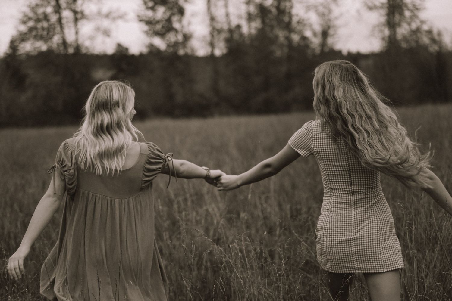Friends hold hands while walking through a field in black and white photography.