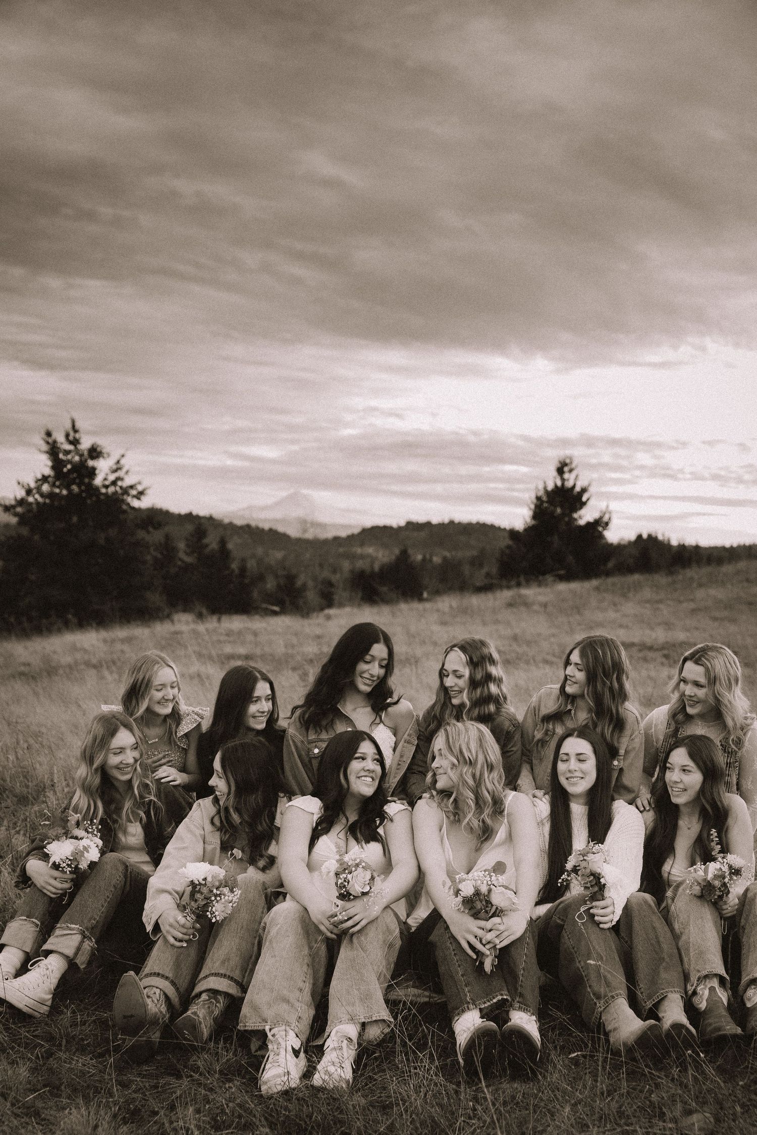 A black and white photograph of a group sitting together on a grassy hillside under a cloudy sky.