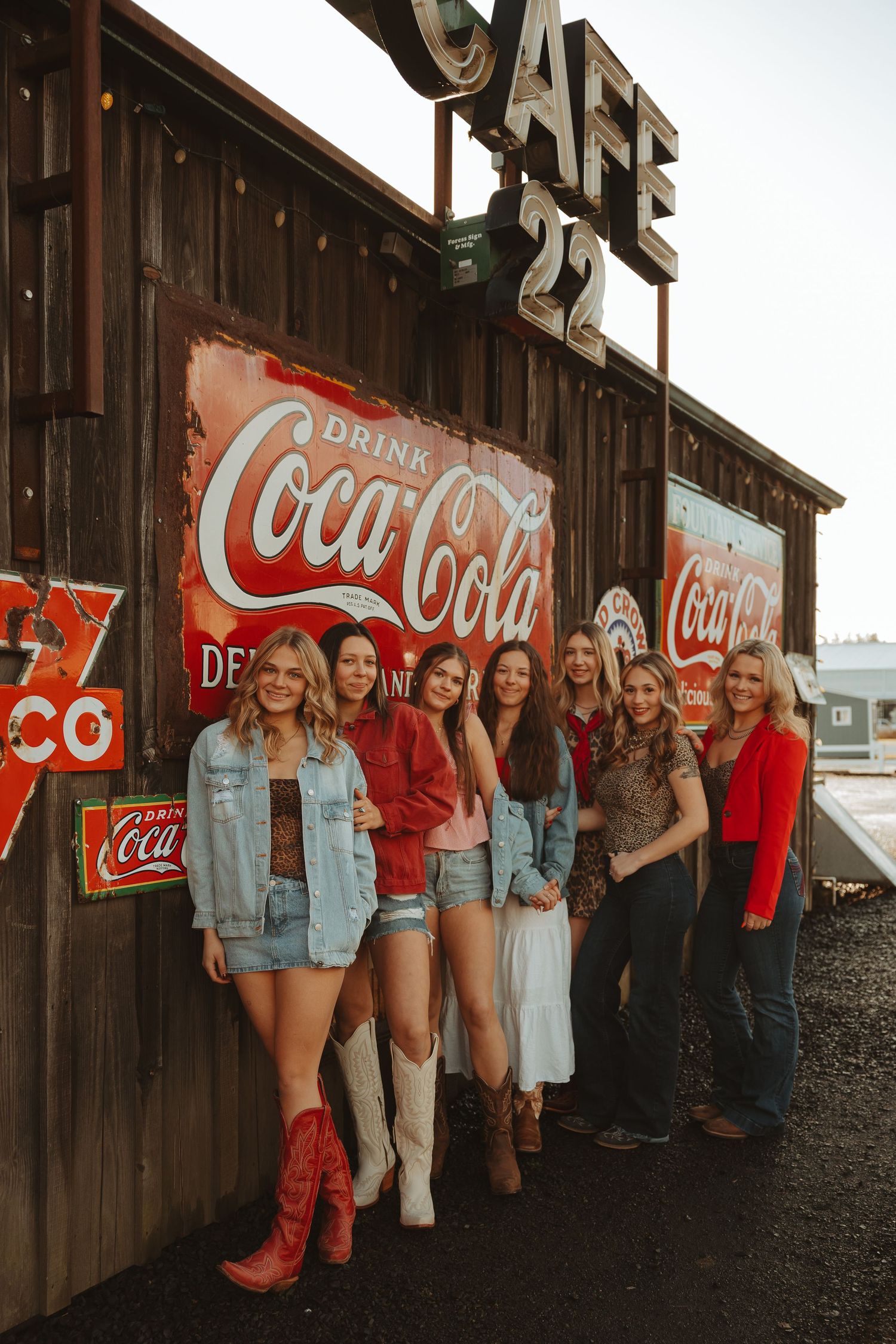 Group of women posing by vintage Coca-Cola signs on rustic wooden wall at Cafe 22, wearing denim and cowboy boots.