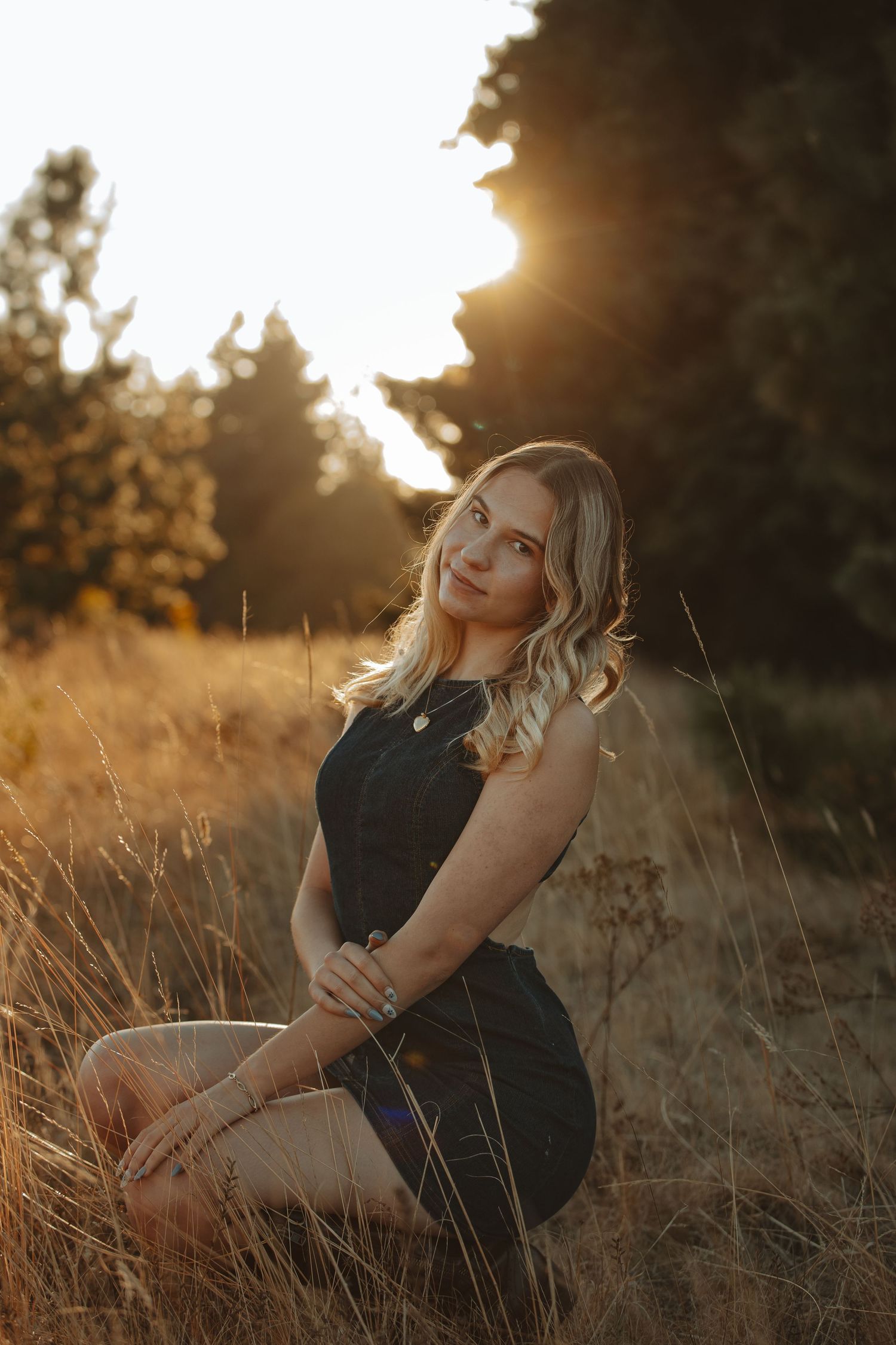 A figure sits in golden sunlit grass during sunset creating a dreamy outdoor portrait series.