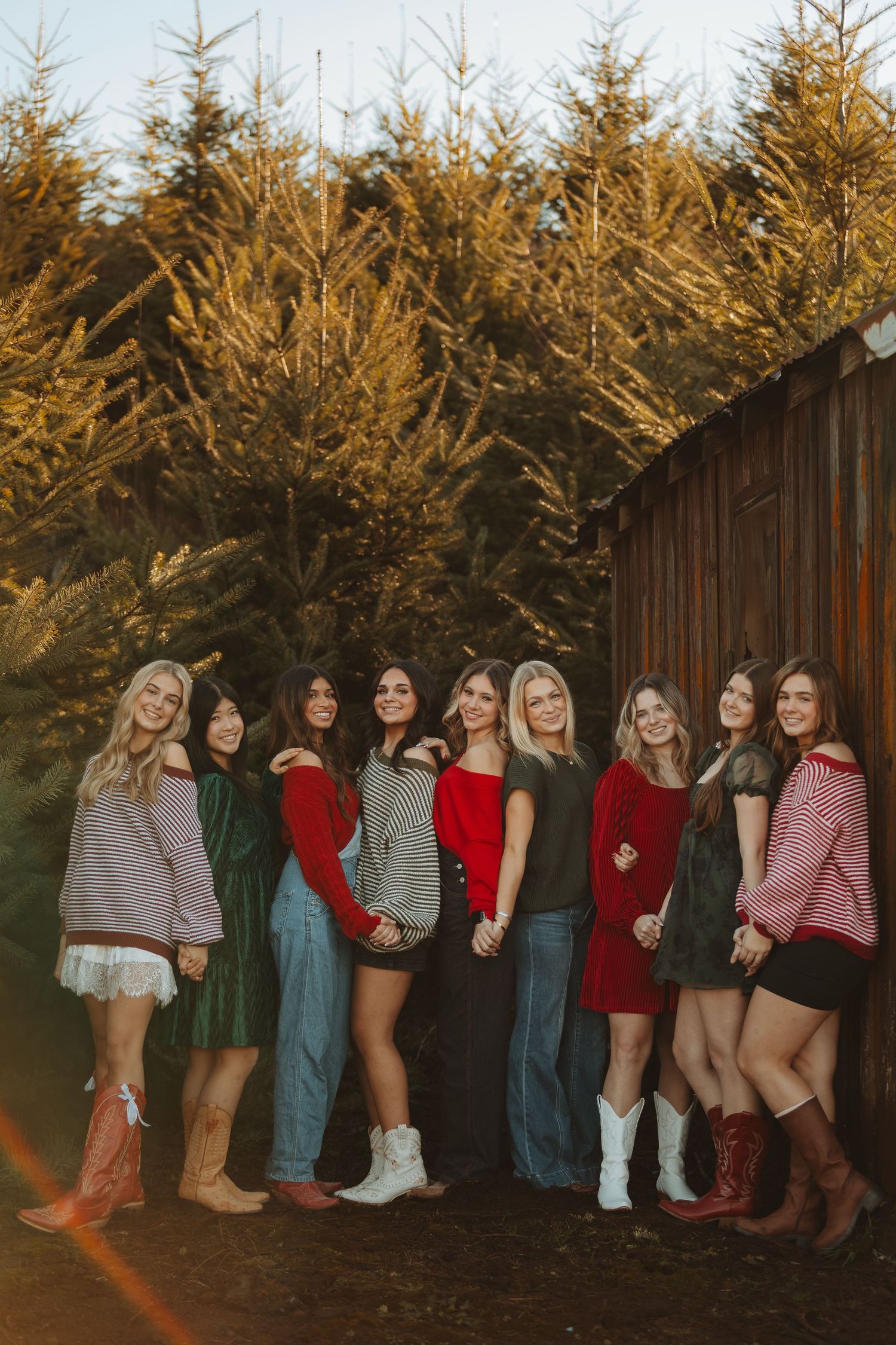 Friends in winter outfits and boots line up against rustic barn wall at golden hour.
