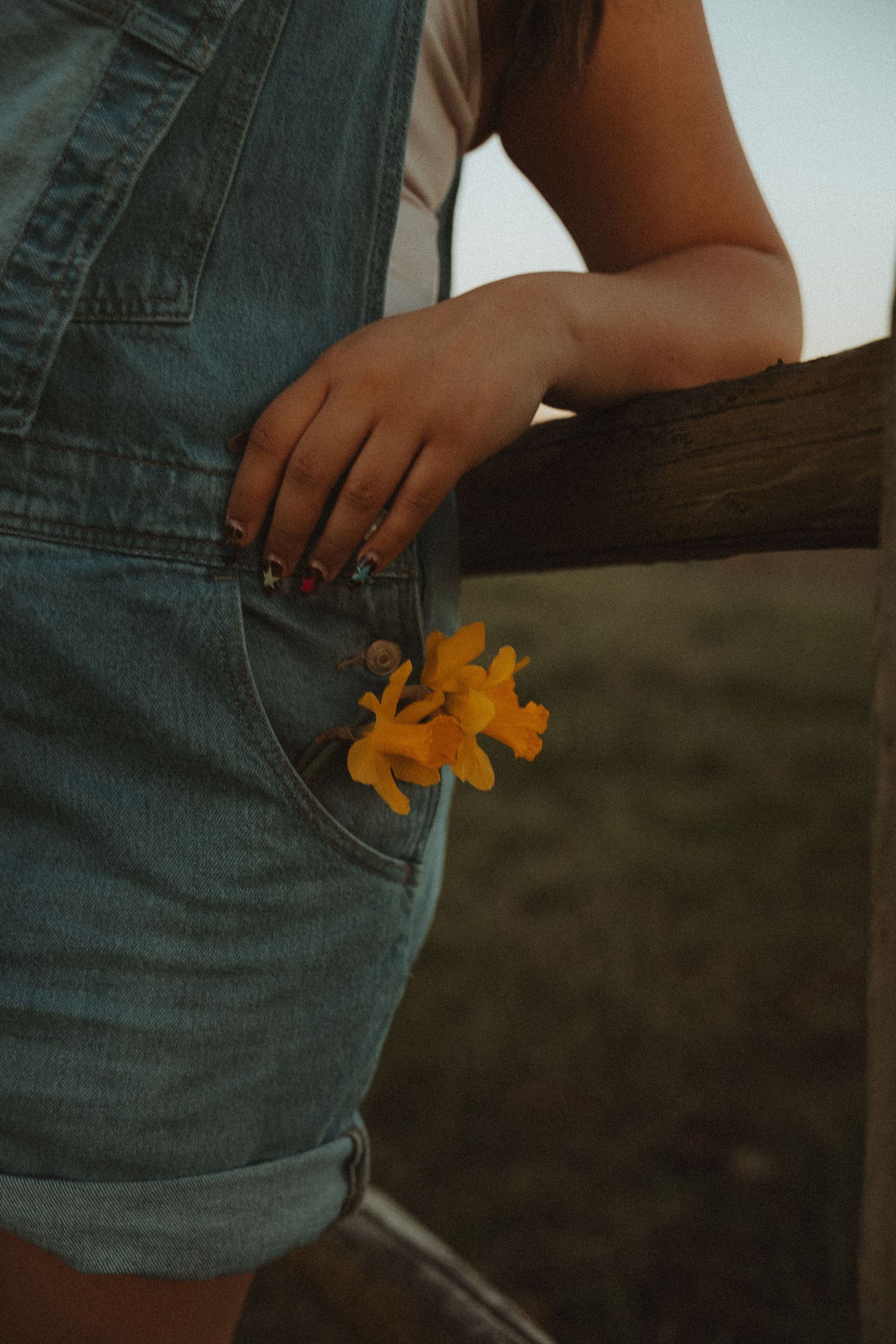 Close-up of denim overall shorts pocket with yellow flowers at golden hour.