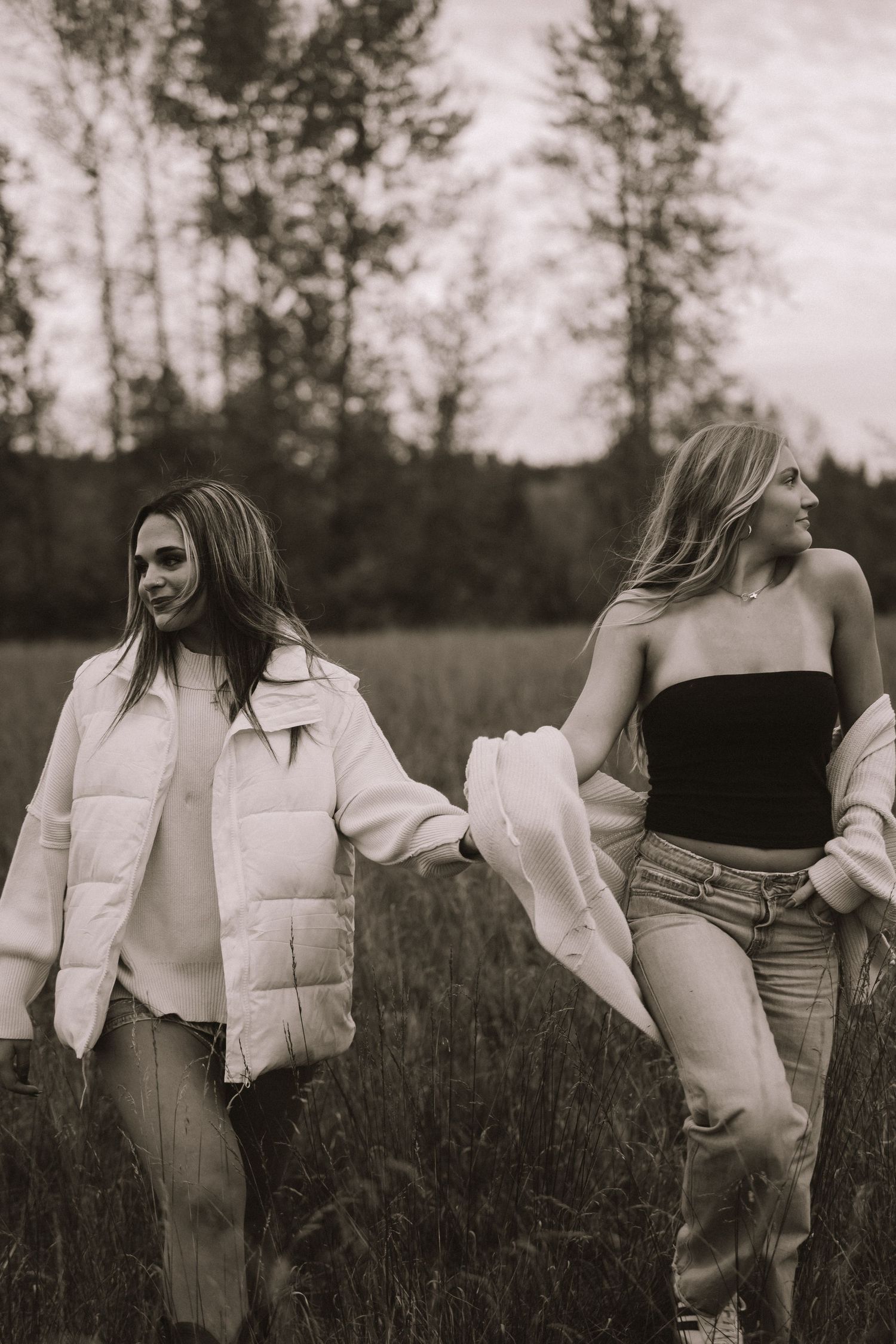 Two friends in casual outfits walk through a grassy field at dusk, captured in black and white photography.