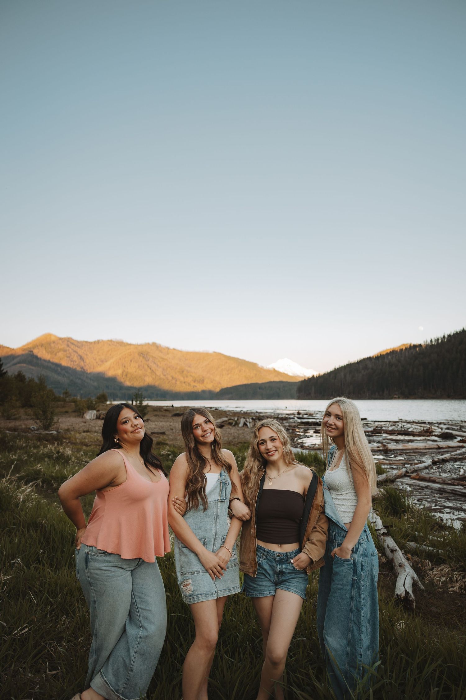 Four young women posing together by a mountain lake during golden hour sunset.