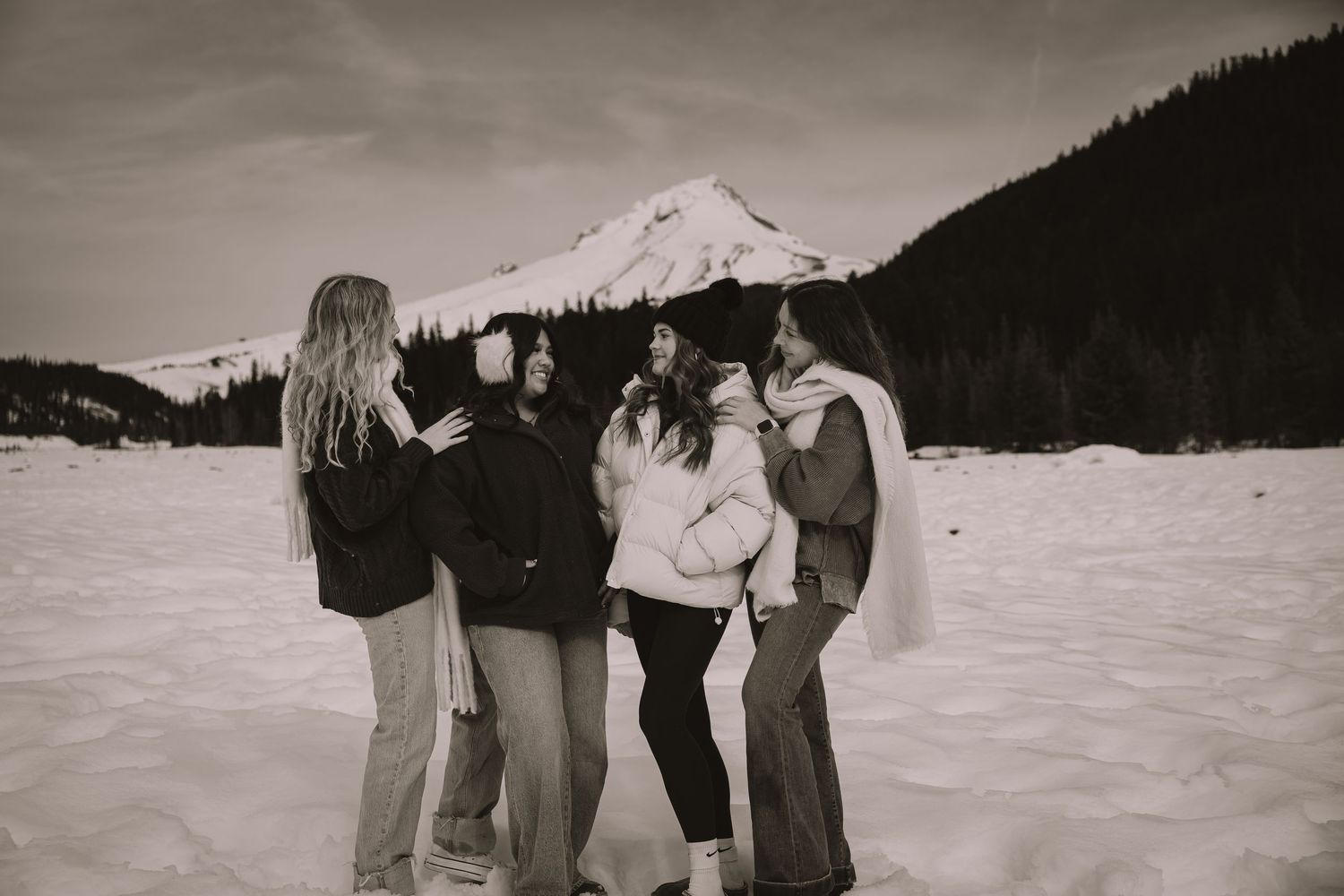 Five friends embrace in a snowy winter landscape with a mountain peak in the background, captured in sepia tone.