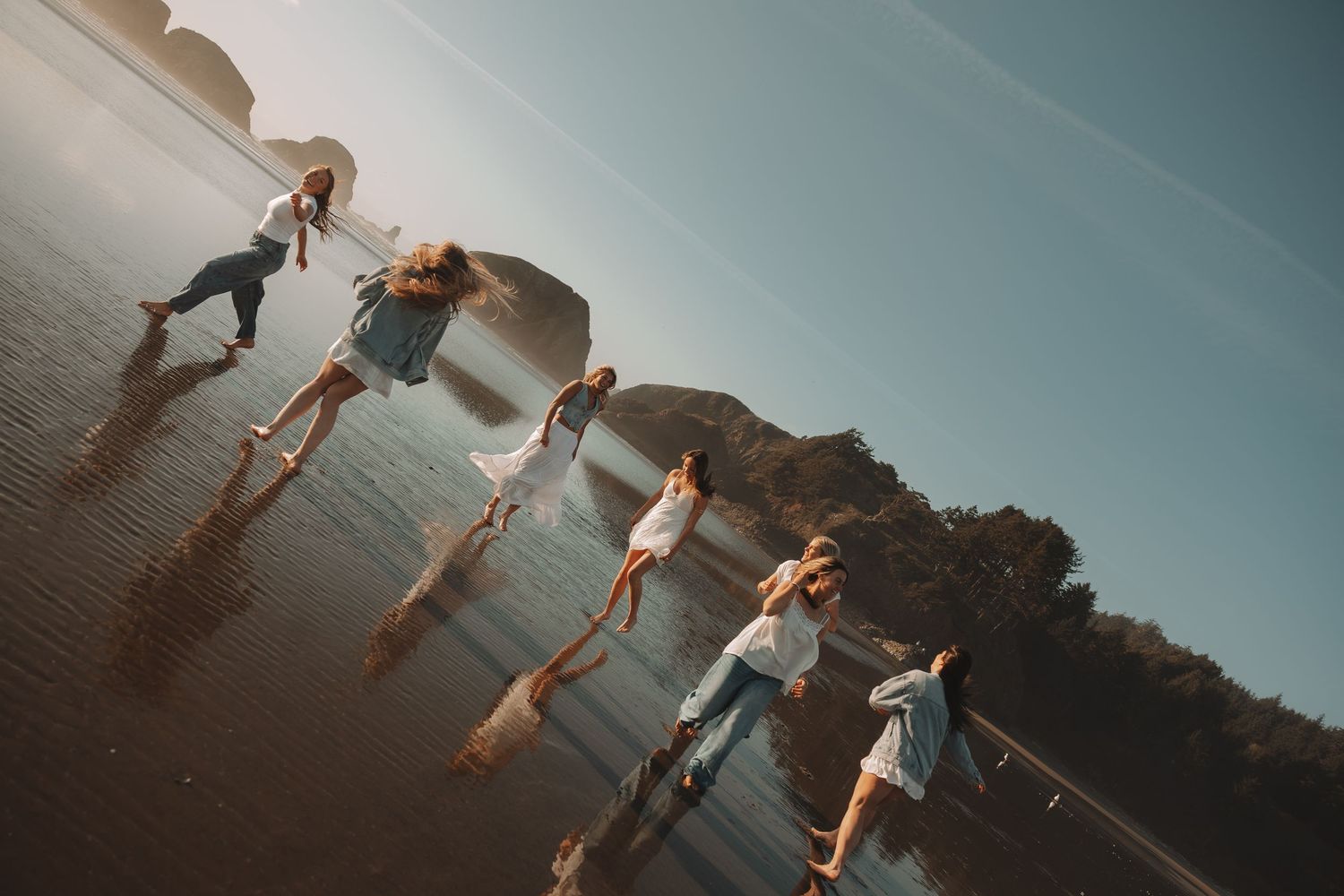 Group of friends walking on a reflective wet beach at sunset with rocky cliffs in the background.
