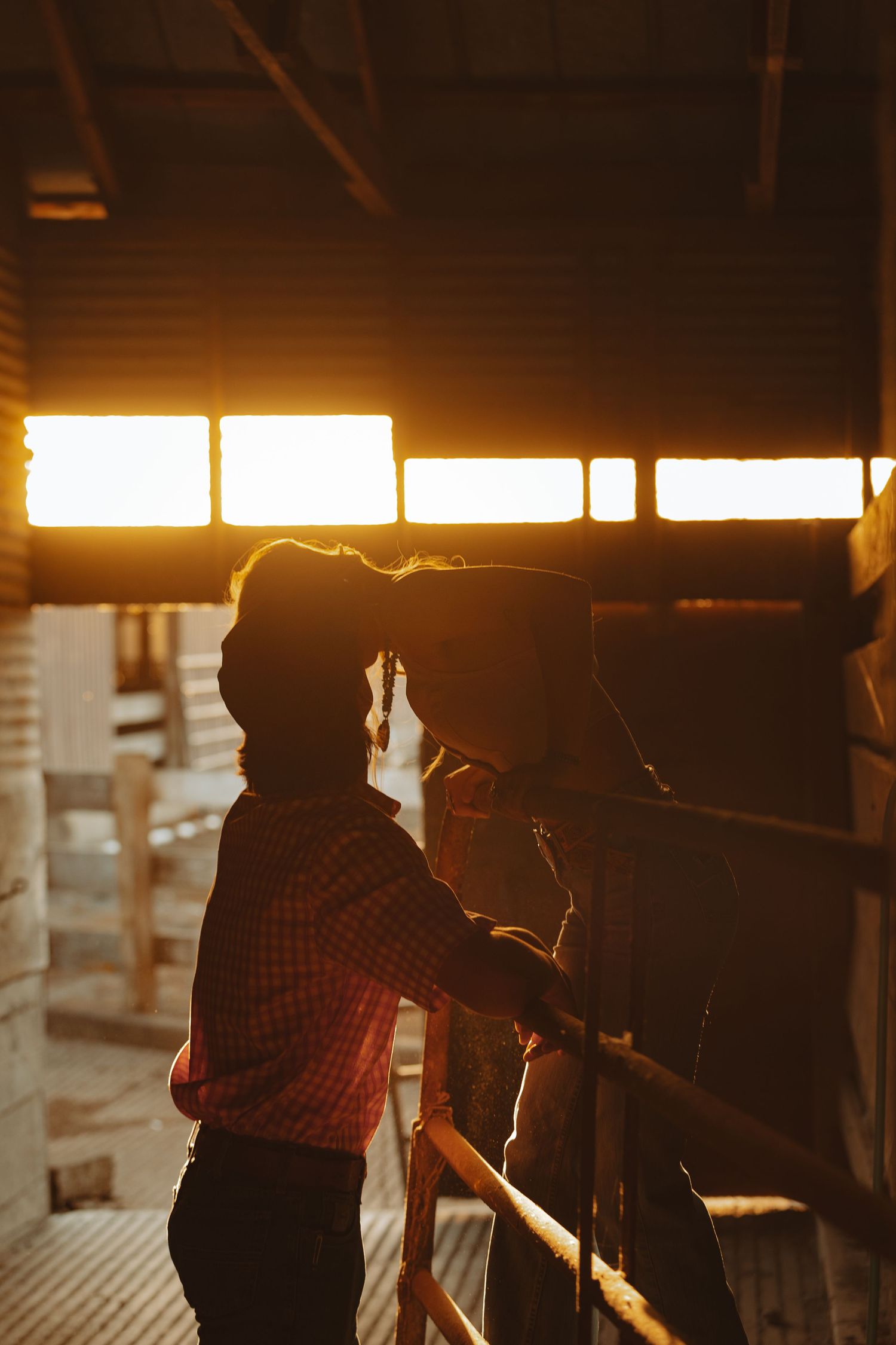 Couple sharing a romantic moment in a golden sunset-lit barn stable with warm glowing light.