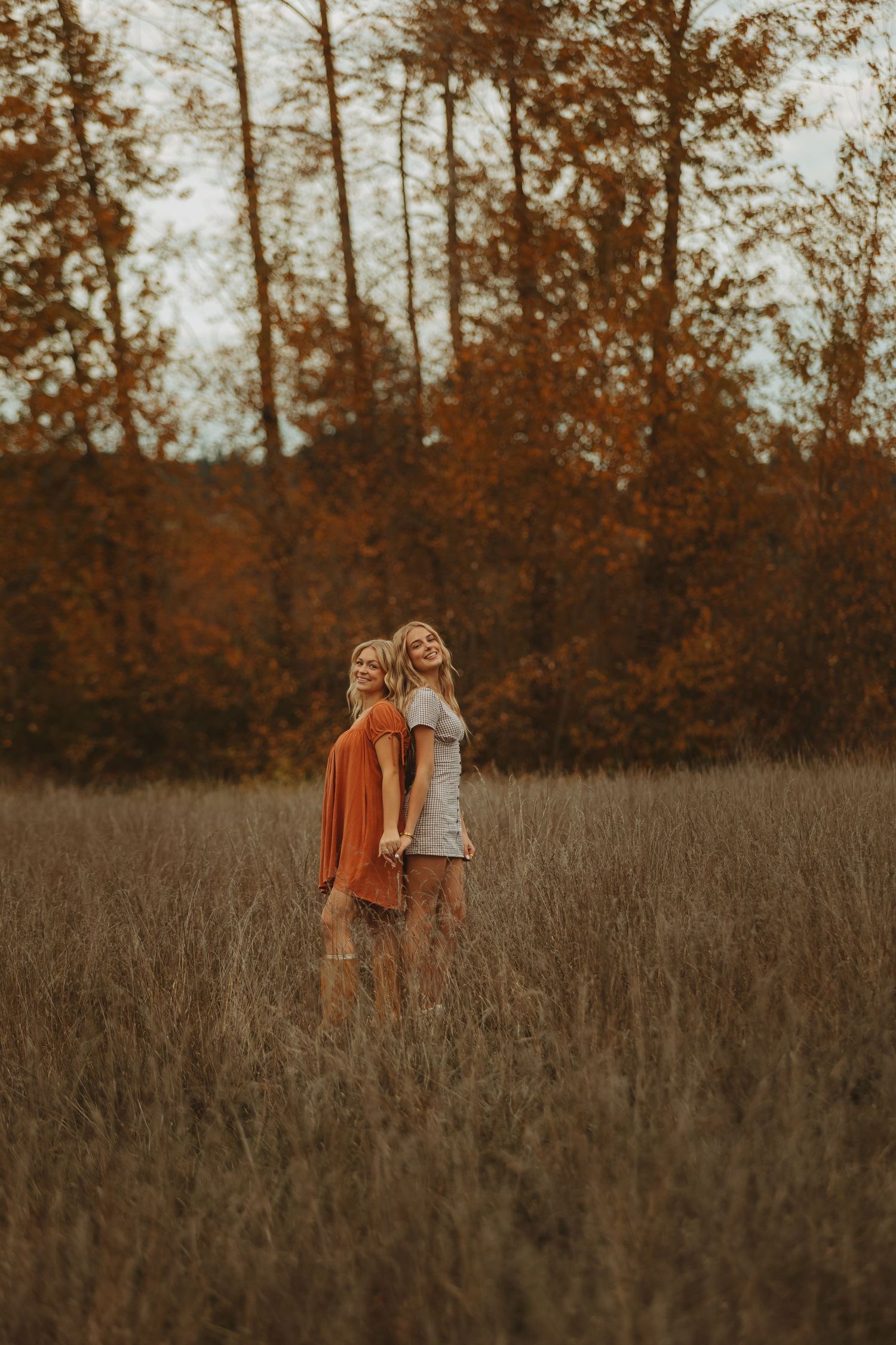 Two people in autumn colors embrace in a golden field during sunset.