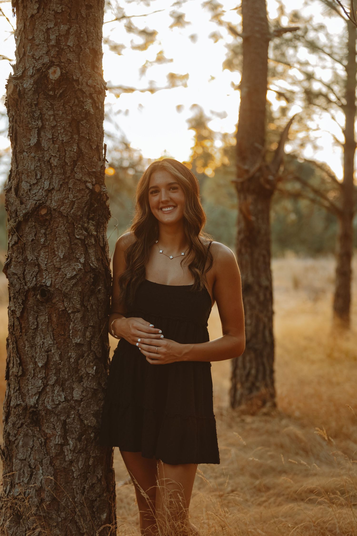Two people laughing together in a pine forest at golden hour with warm sunlight filtering through the trees.