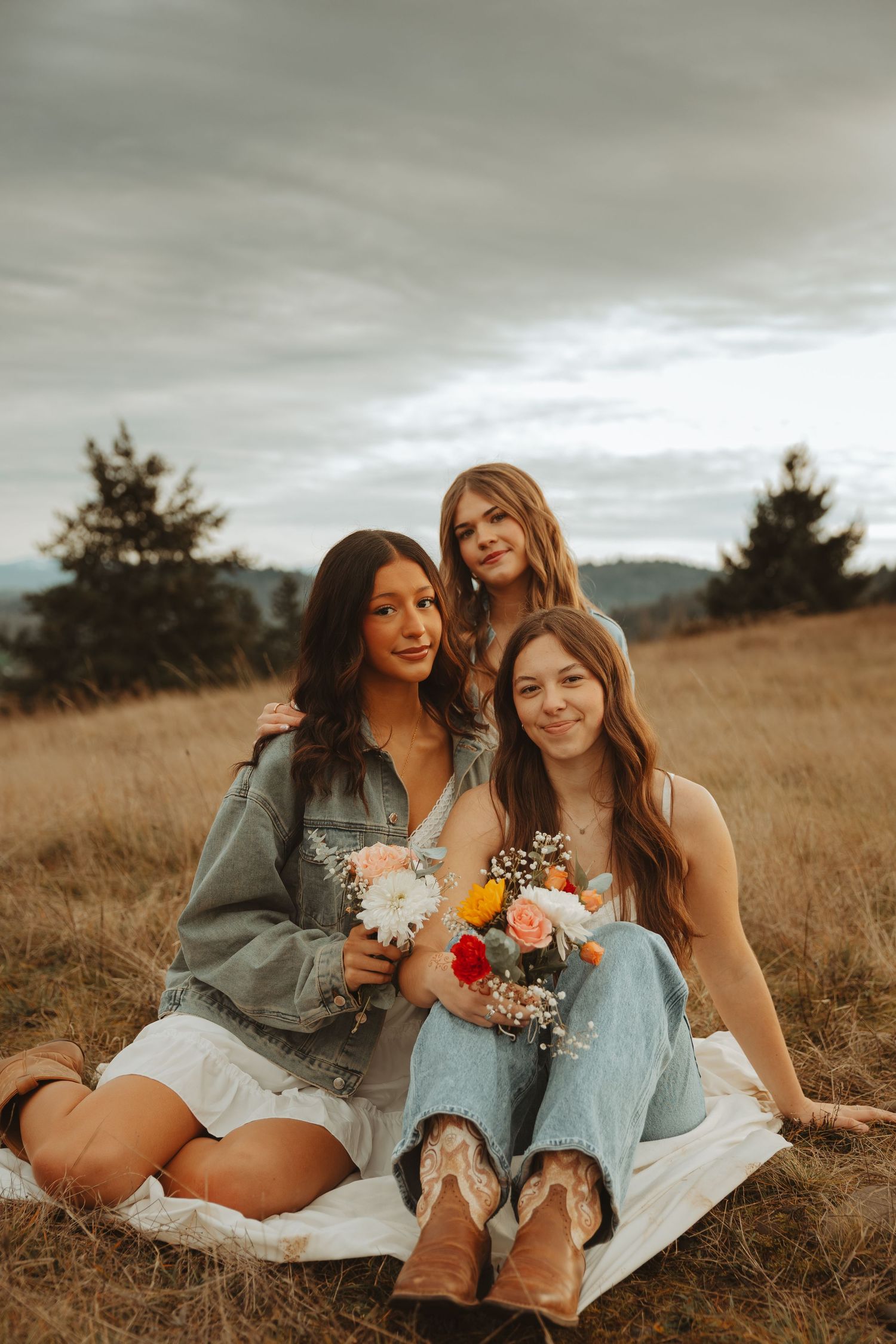 A group of friends hold flowers while relaxing in casual outfits on a grassy hillside.