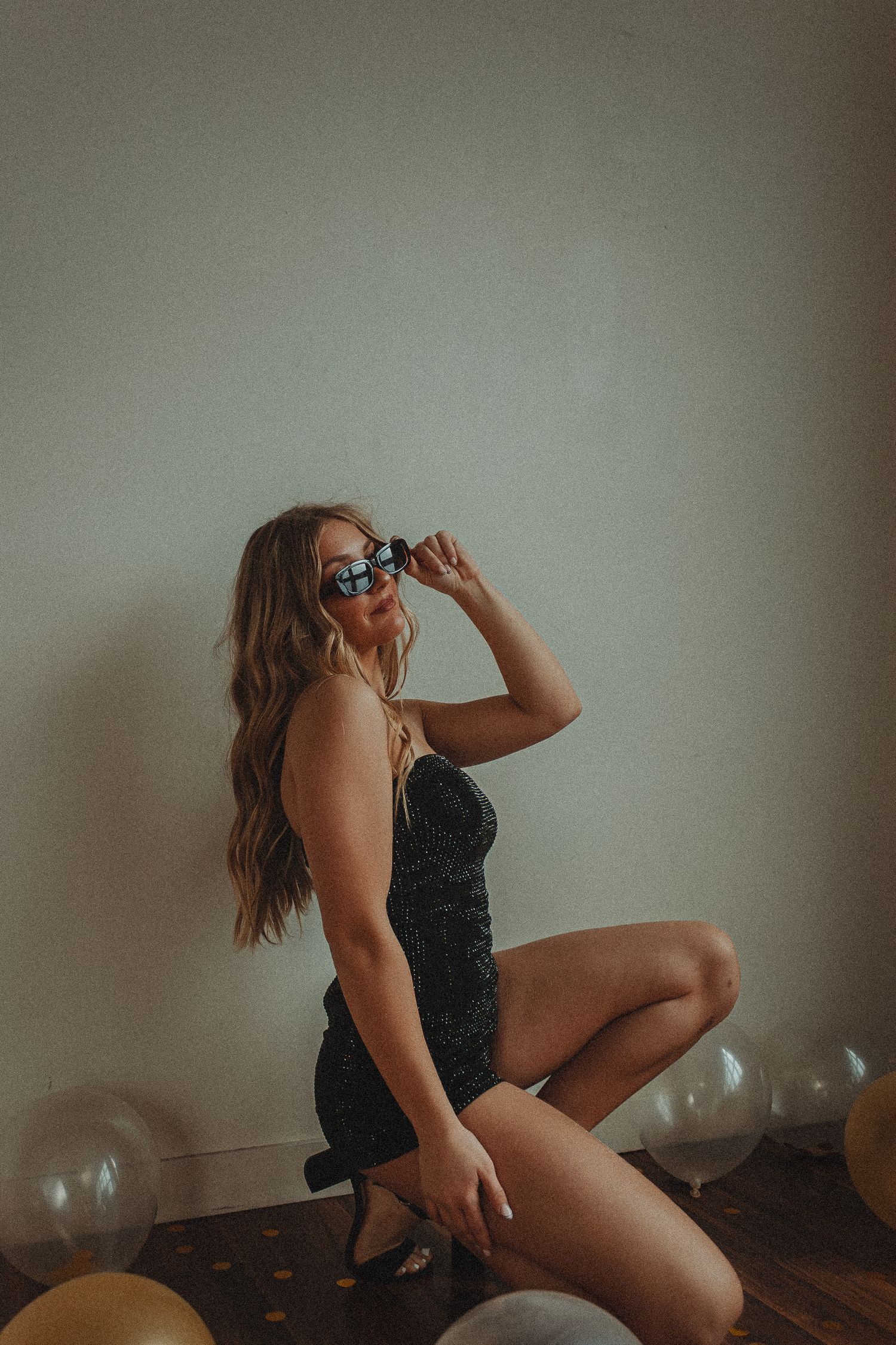 Figure poses artistically with balloons in moody indoor photoshoot setting.