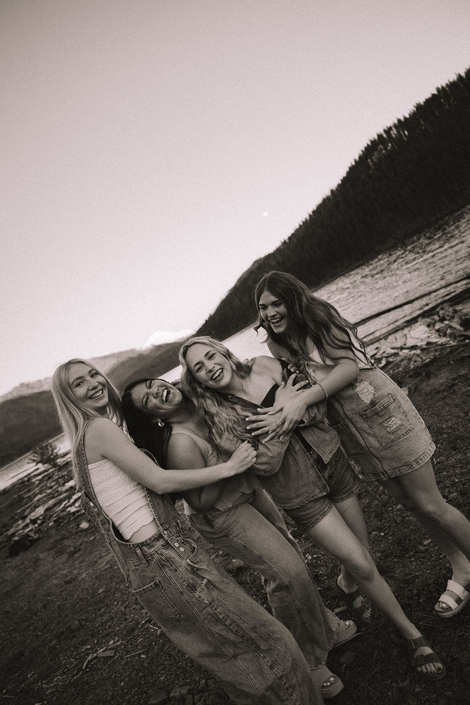 Black and white photo of four laughing young women embracing by a mountain lake.